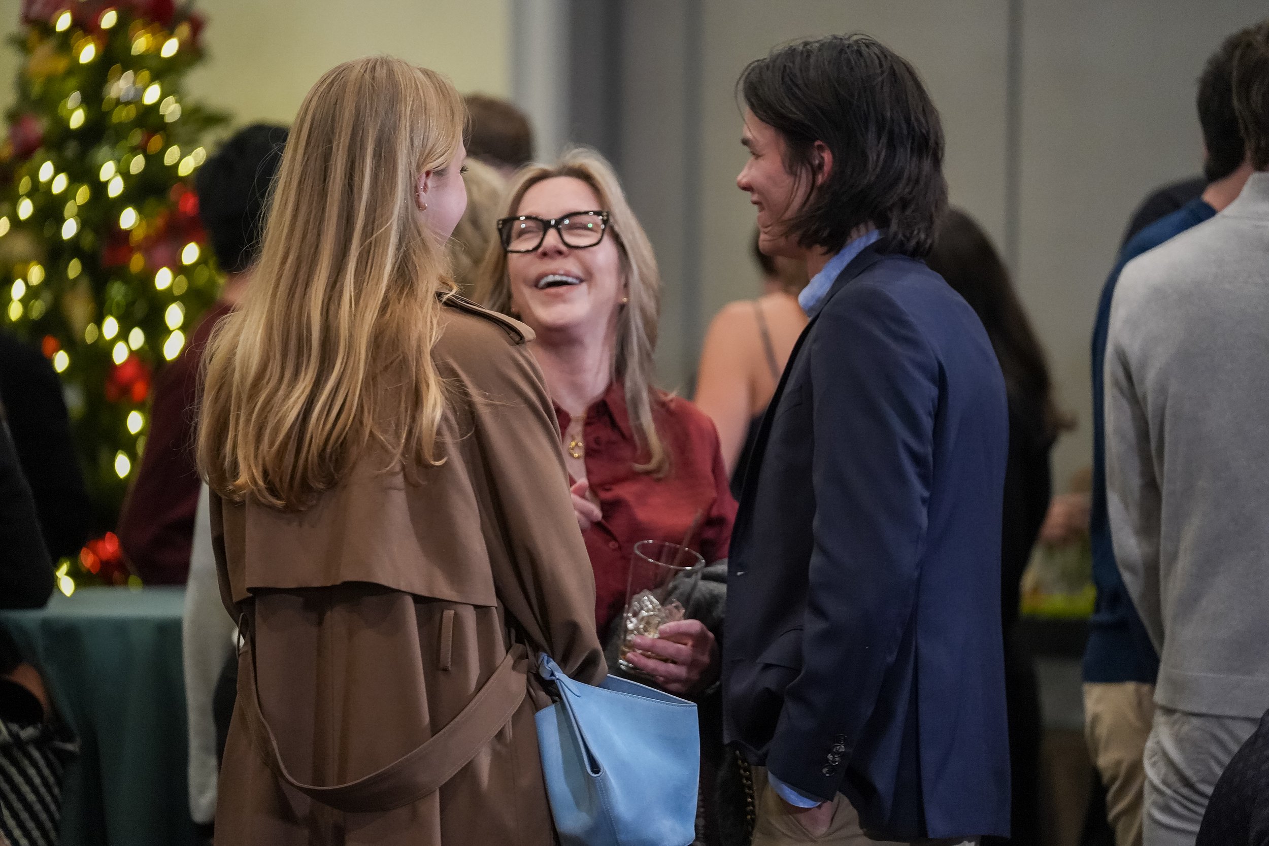 People socializing at a holiday event with a Christmas tree in the background.