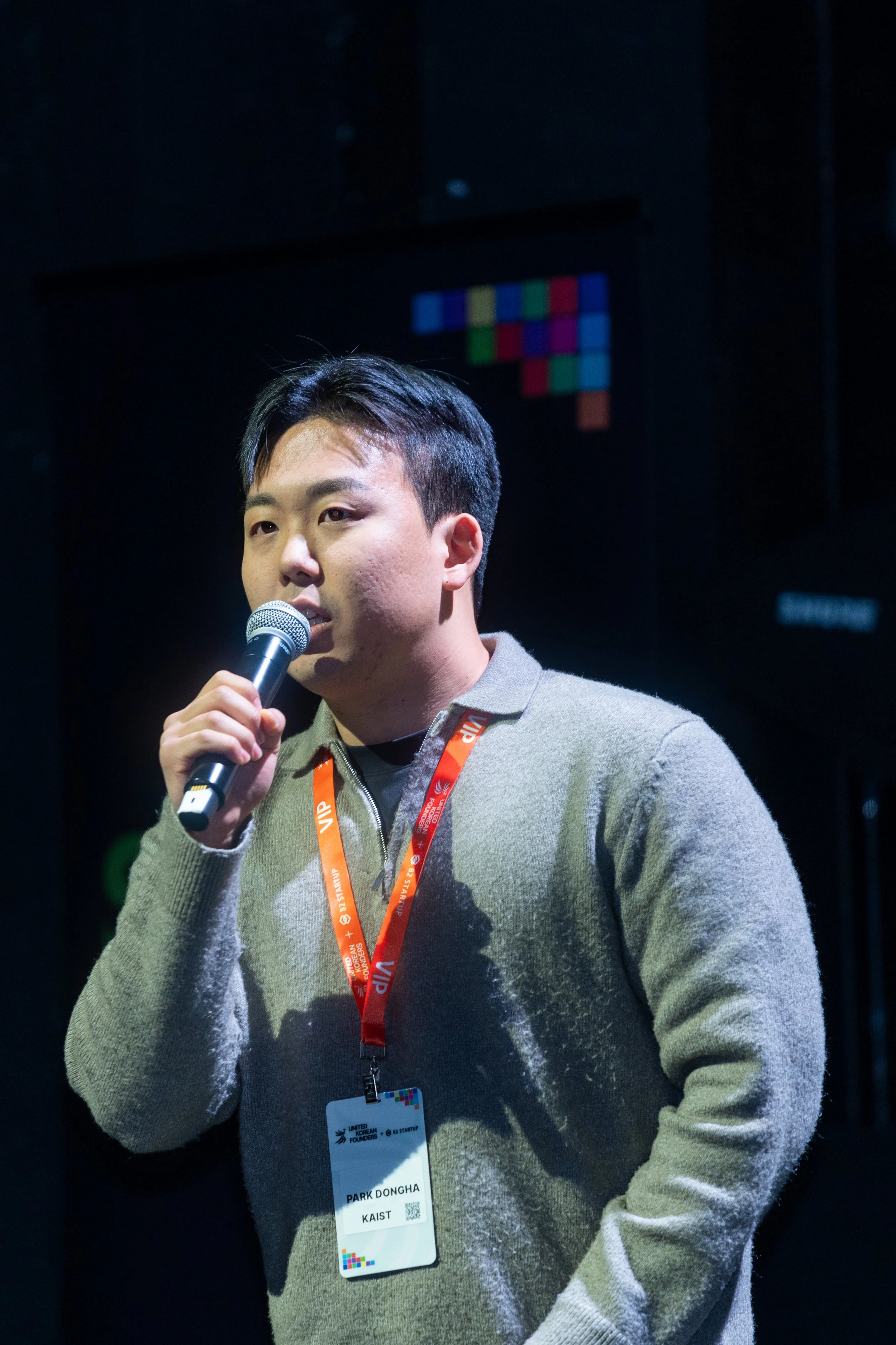 Person speaking into a microphone at an event with a badge.