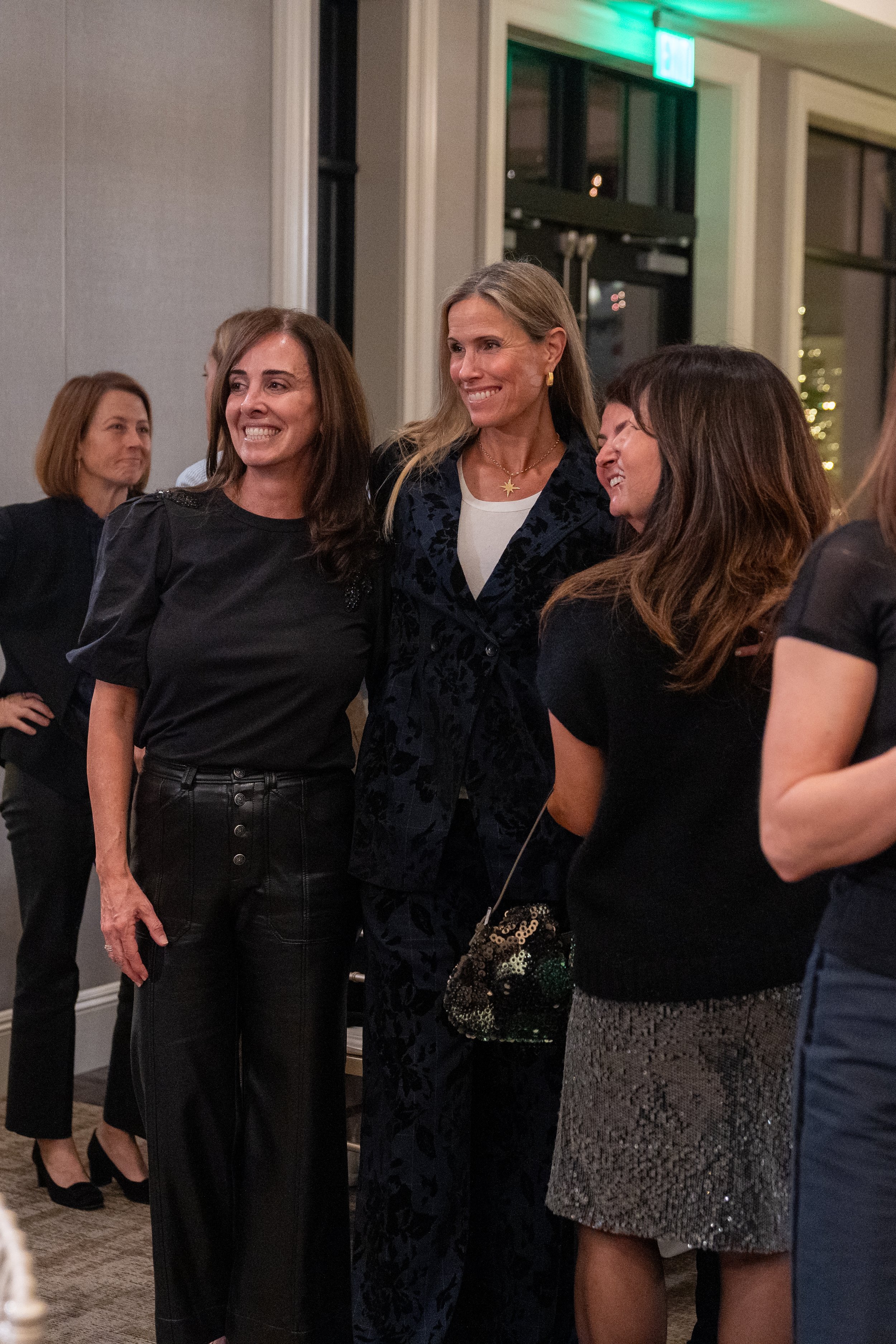 Group of women smiling and interacting at an indoor event, dressed in semi-formal attire.