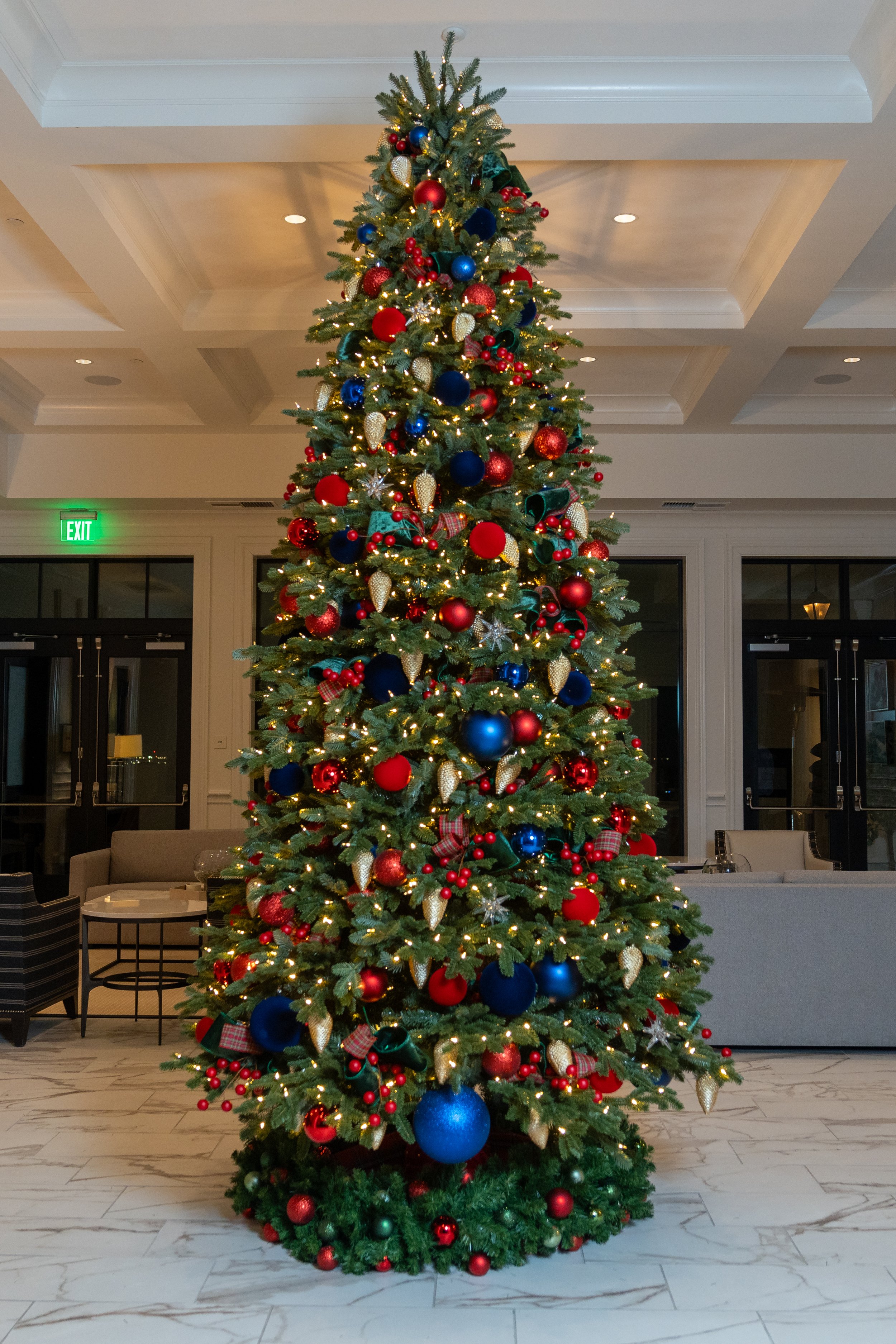 Tall Christmas tree with red, blue, and gold ornaments in a lobby.