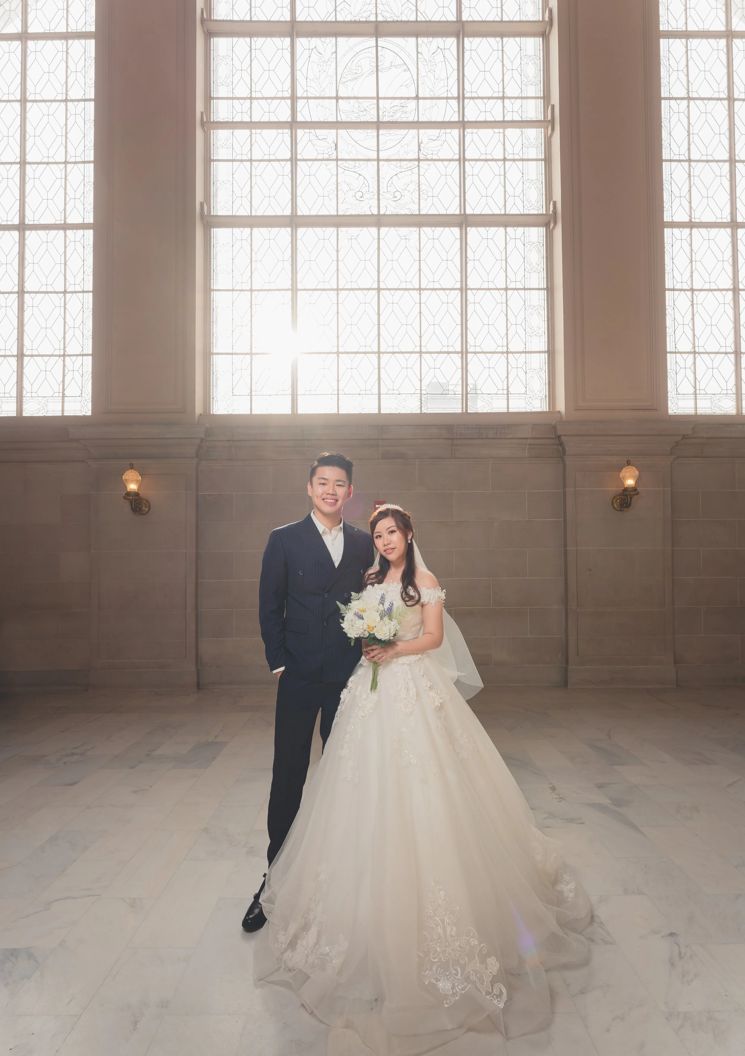 Bride and groom posing together inside San Francisco City Hall with natural light from the historic windows.