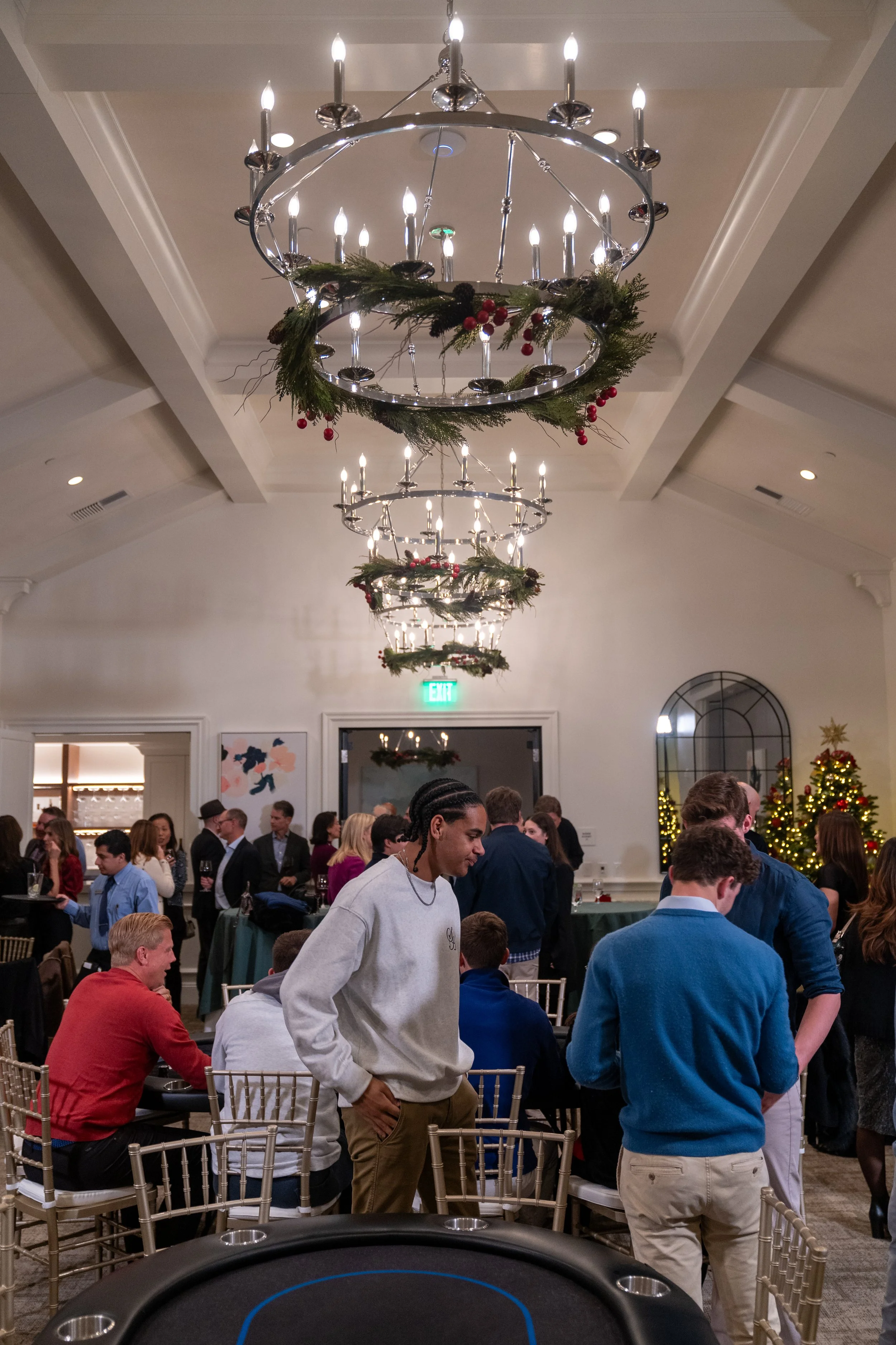 People at a holiday party in a decorated indoor venue with festive chandeliers and Christmas trees.
