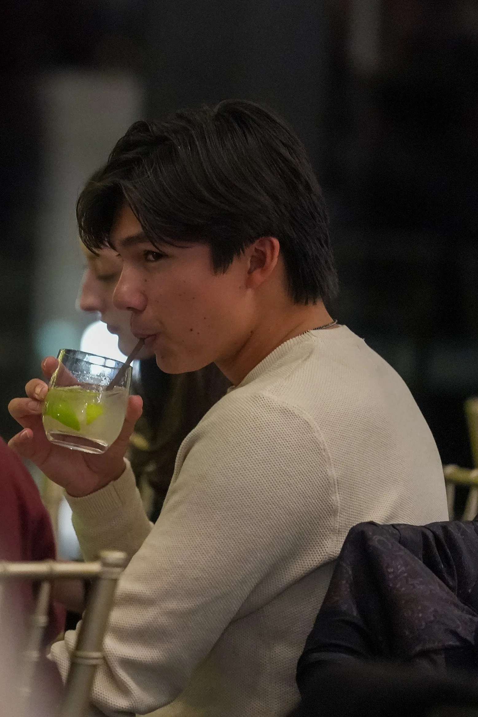 Person wearing a beige sweater drinking from a glass with lime