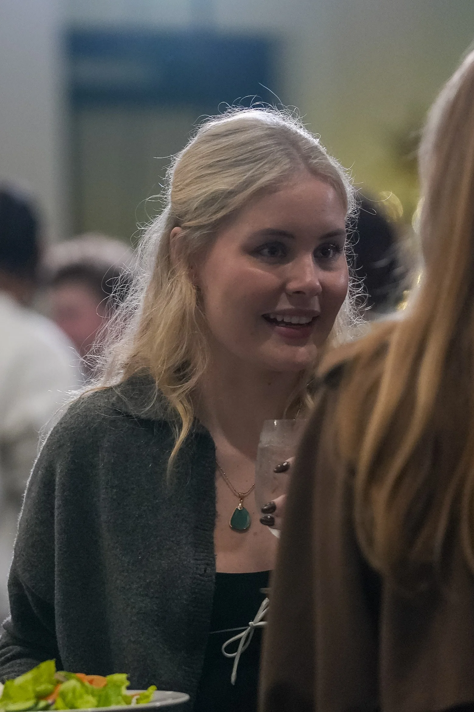 Two women having a conversation at a social gathering, one holding a drink, and the other partially visible.