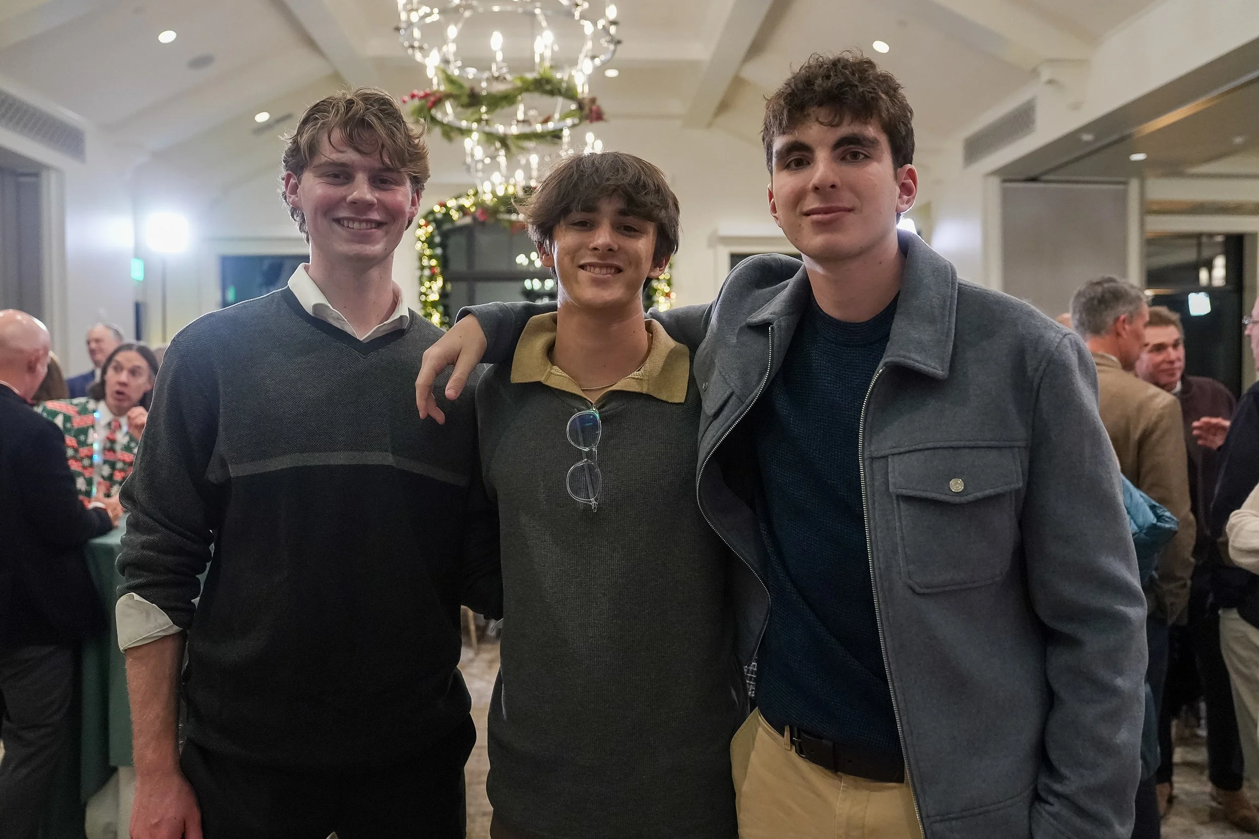 Three young men posing indoors at a social event, with festive holiday decorations in the background.