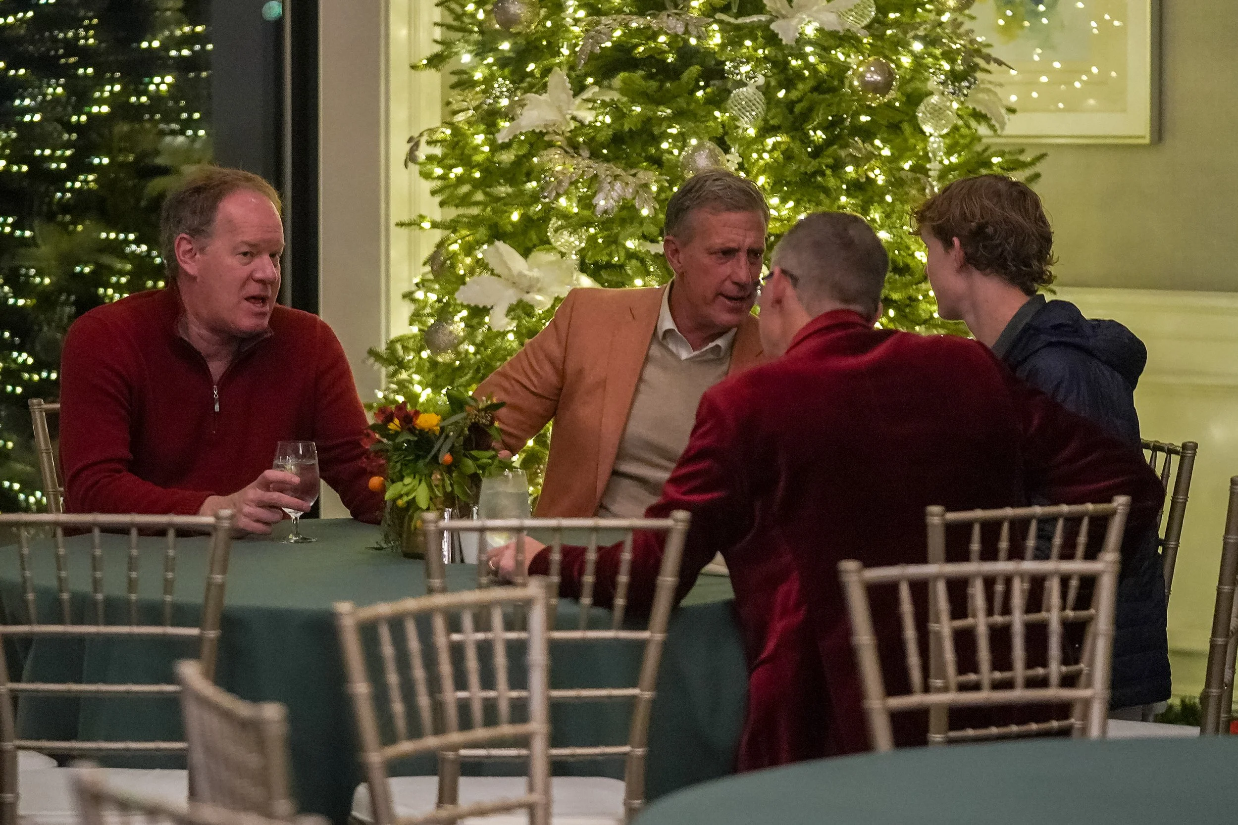 Four people sitting at a table in front of a decorated Christmas tree with lights.
