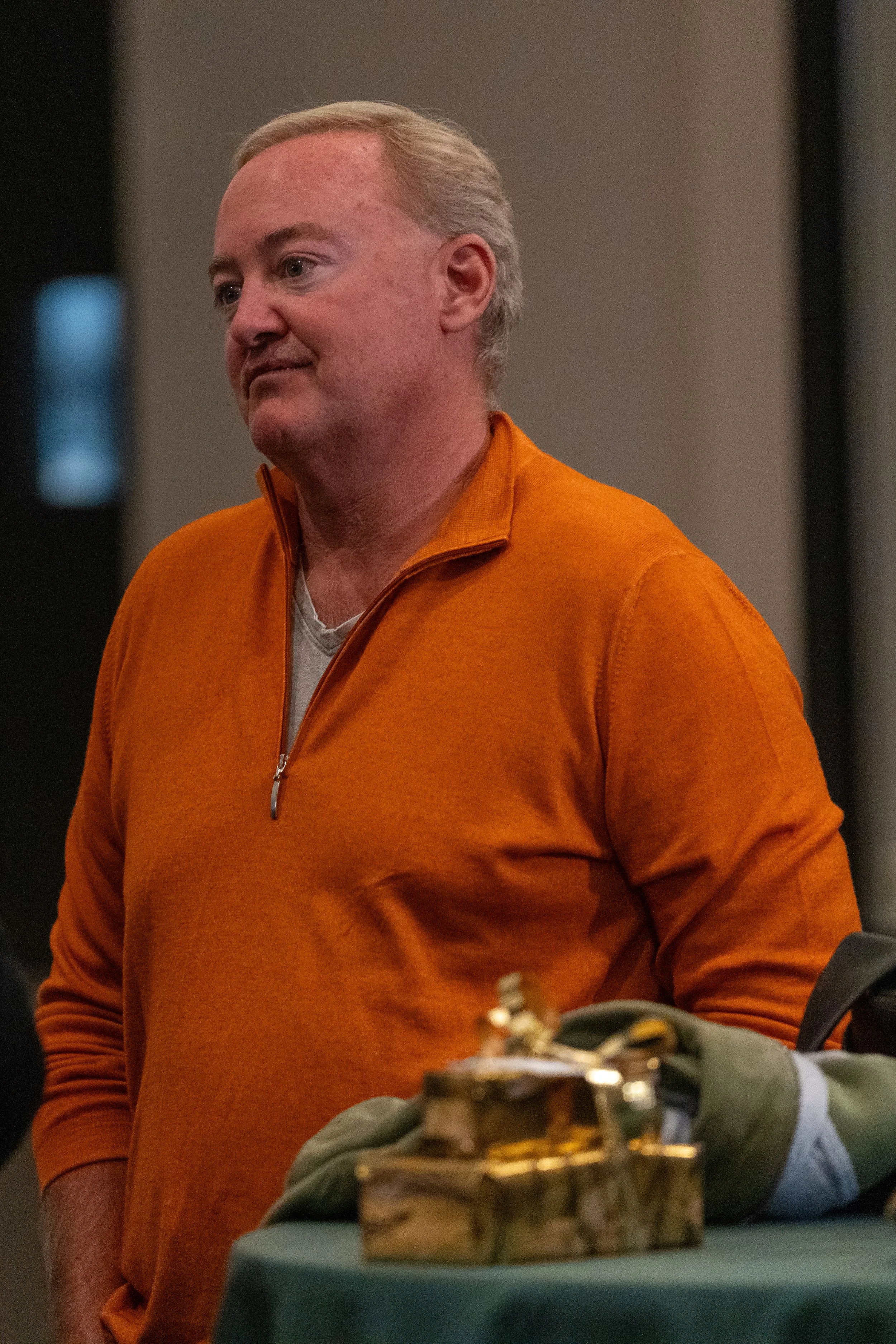 Man in orange sweater standing next to a table with wrapped gifts.