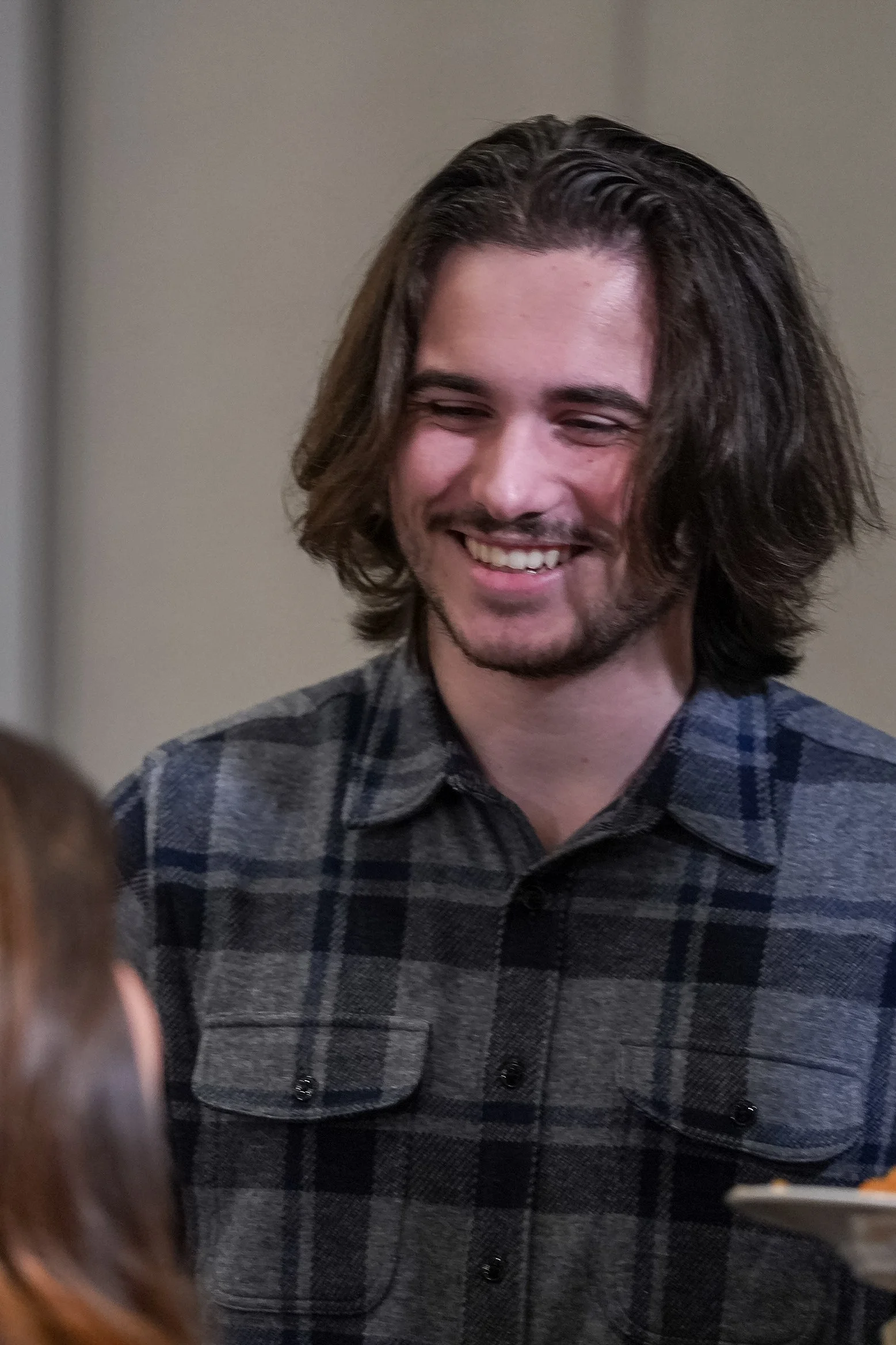 Smiling person with long hair in a plaid shirt.