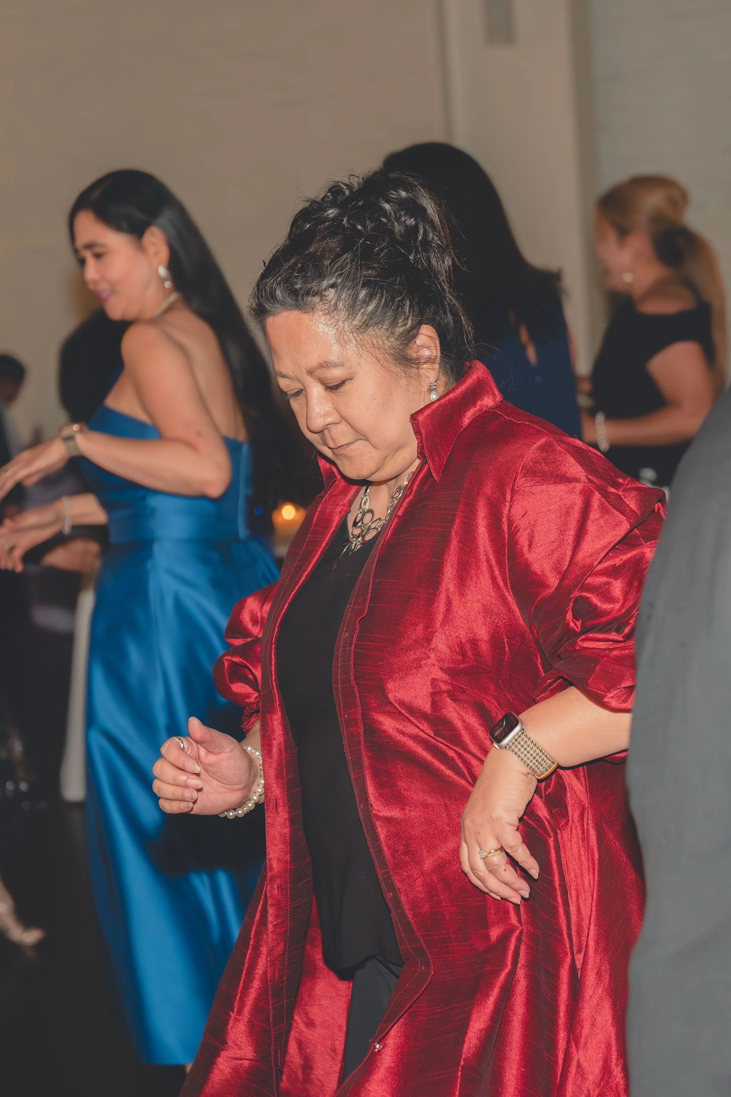 Two women dancing at an indoor event, one wearing a red outfit, and the other in a blue dress.