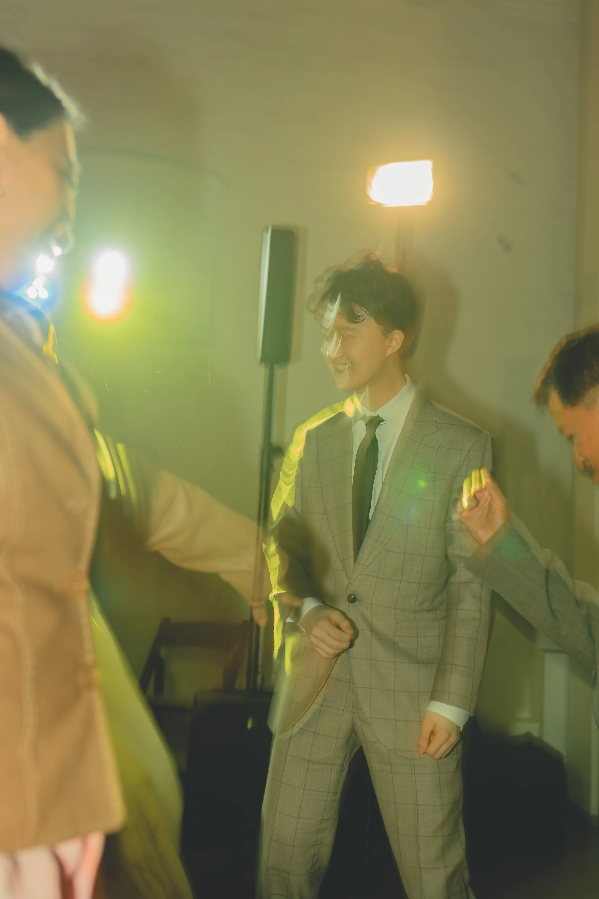 A person in a suit dancing at an event with colorful lighting and other blurred figures around.