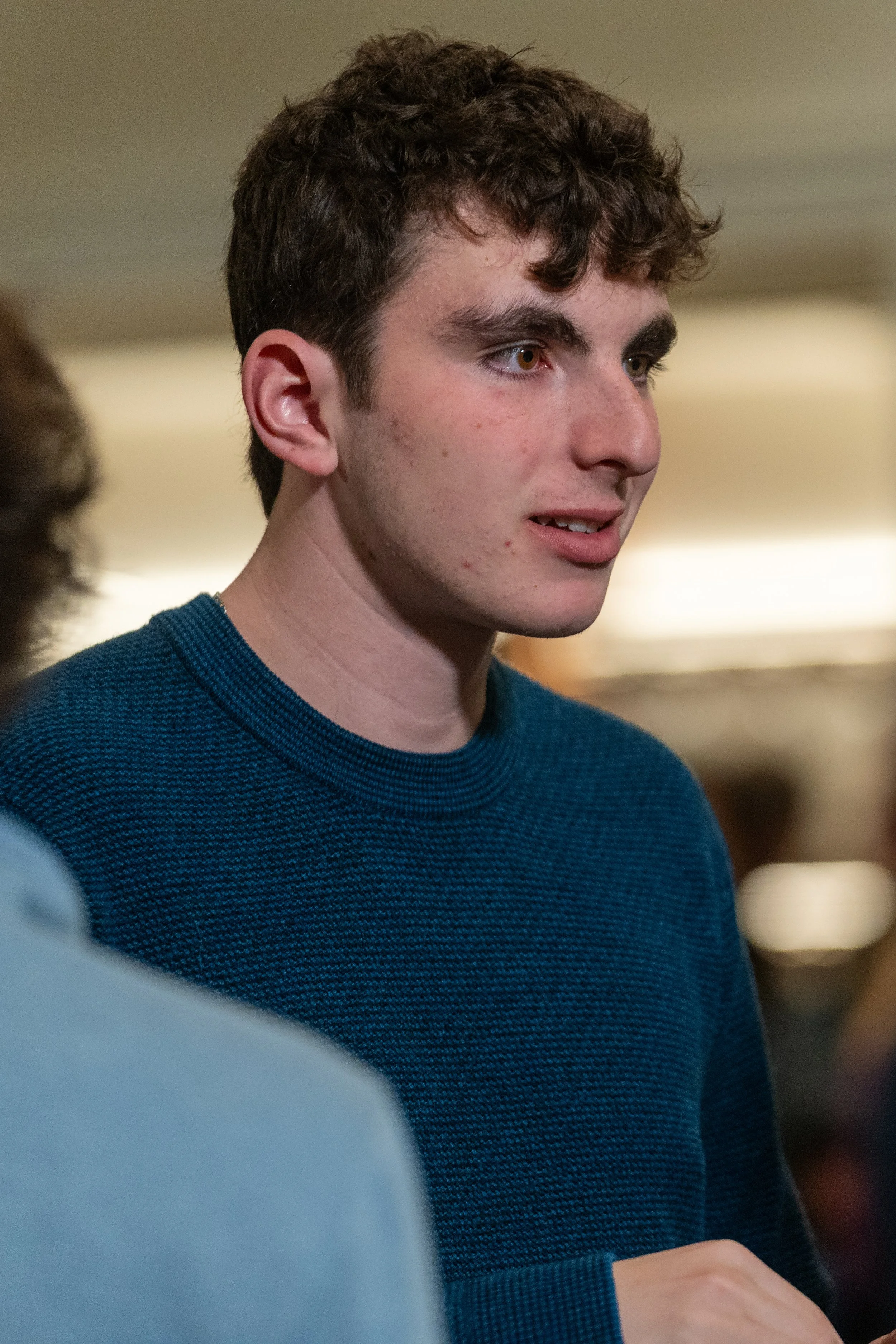 Young man in a blue sweater looking to the side indoors.