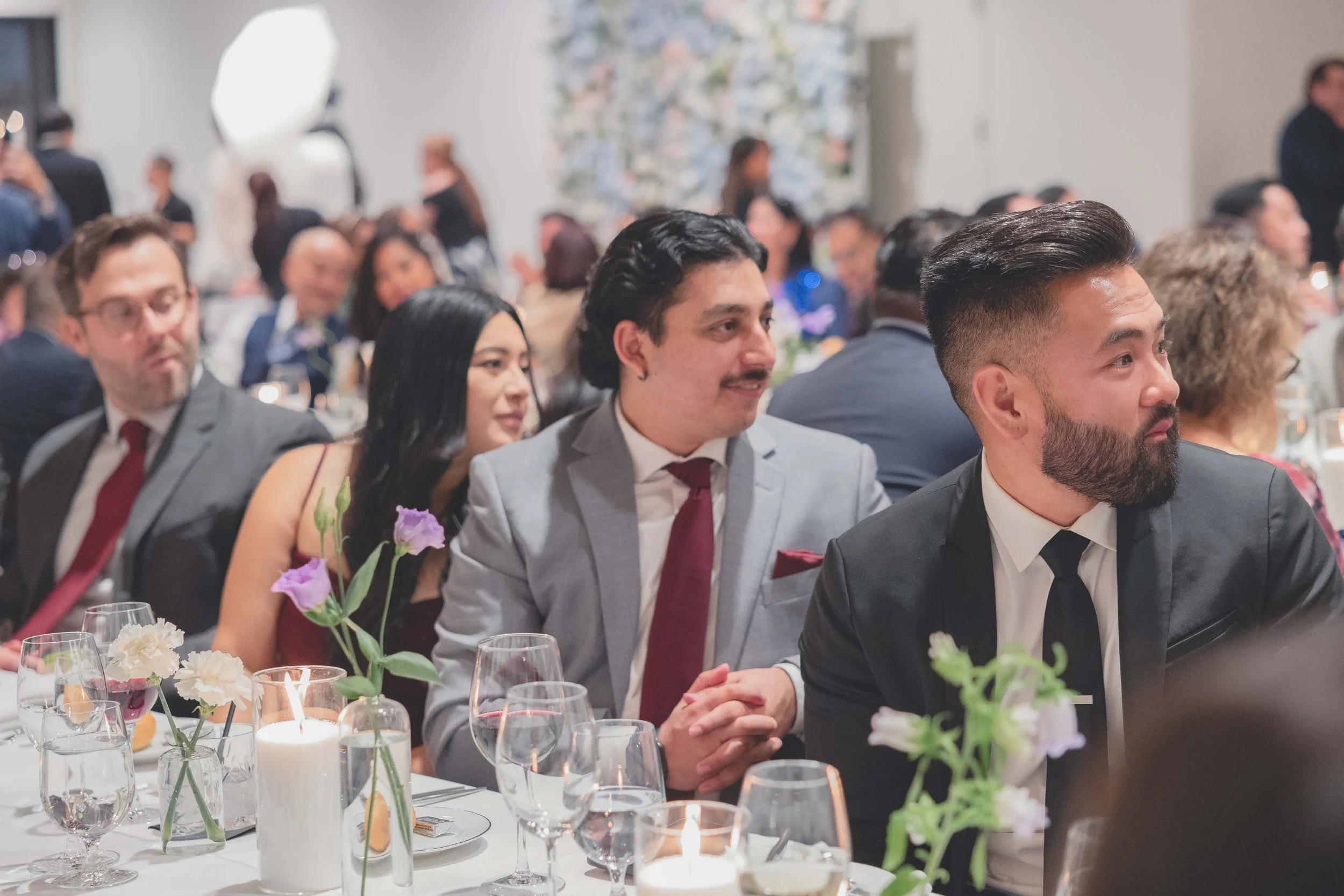 People at a formal event seated at a dining table decorated with candles and flowers.