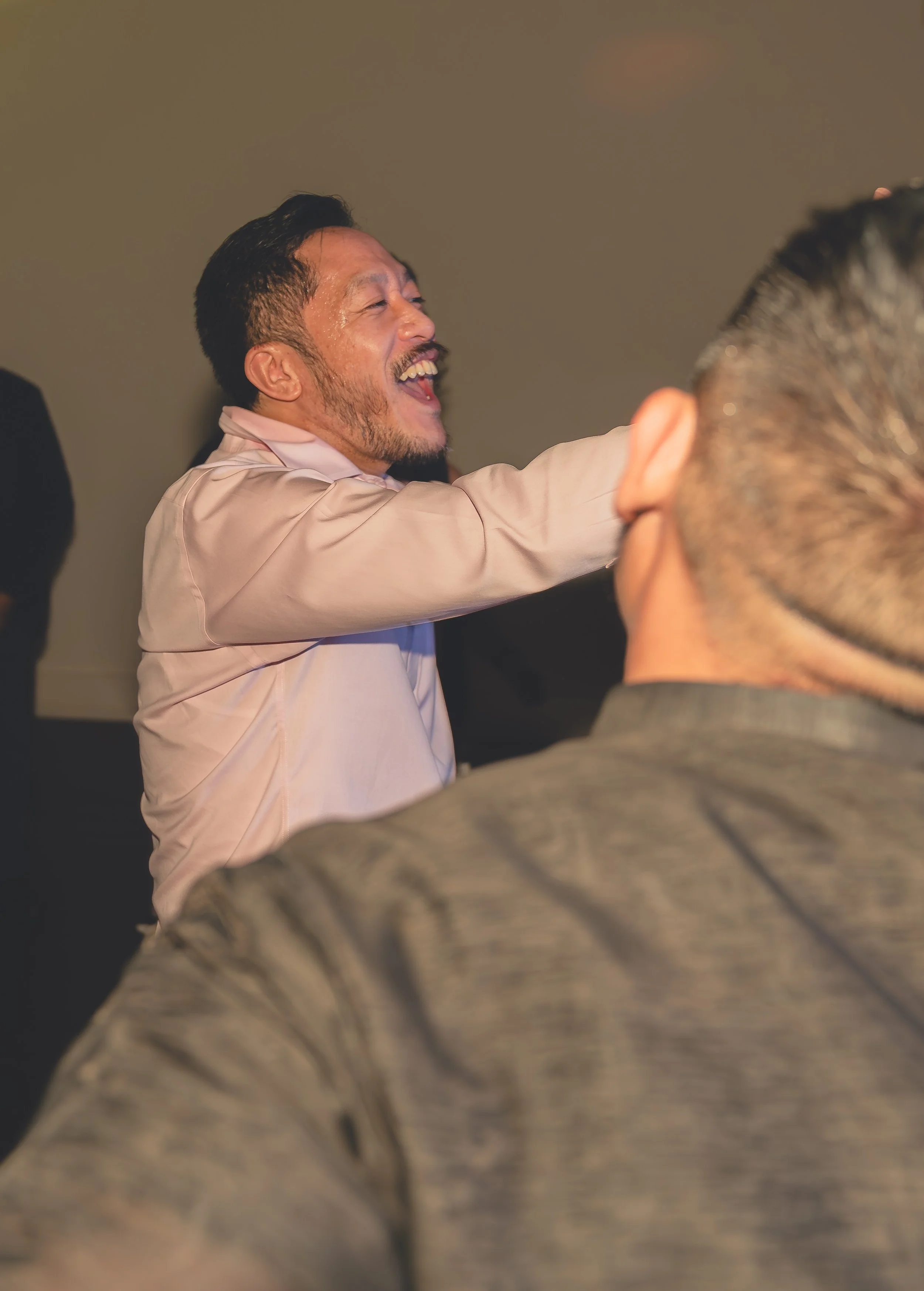 Two men laughing and engaging with others in a lively setting.