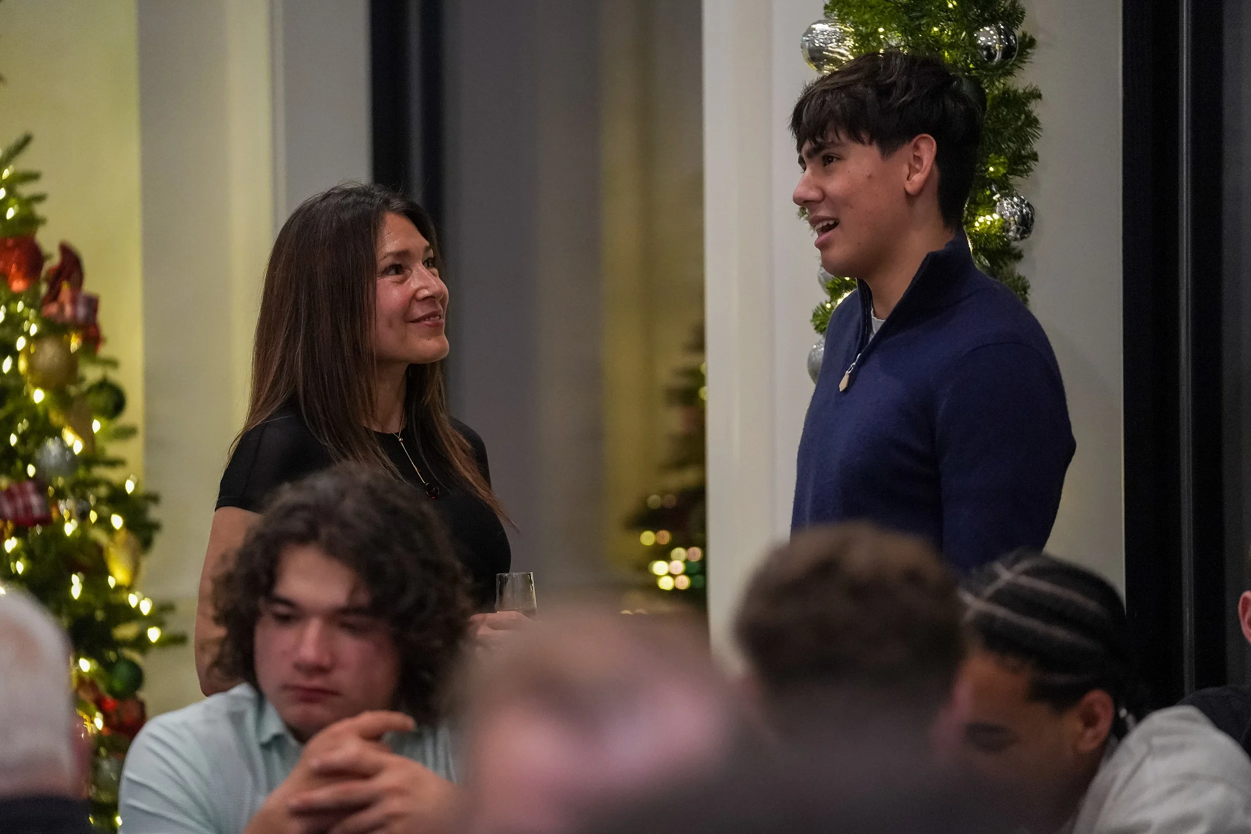 People socializing at a holiday gathering with Christmas decorations, including a lit Christmas tree and garland with silver ornaments.