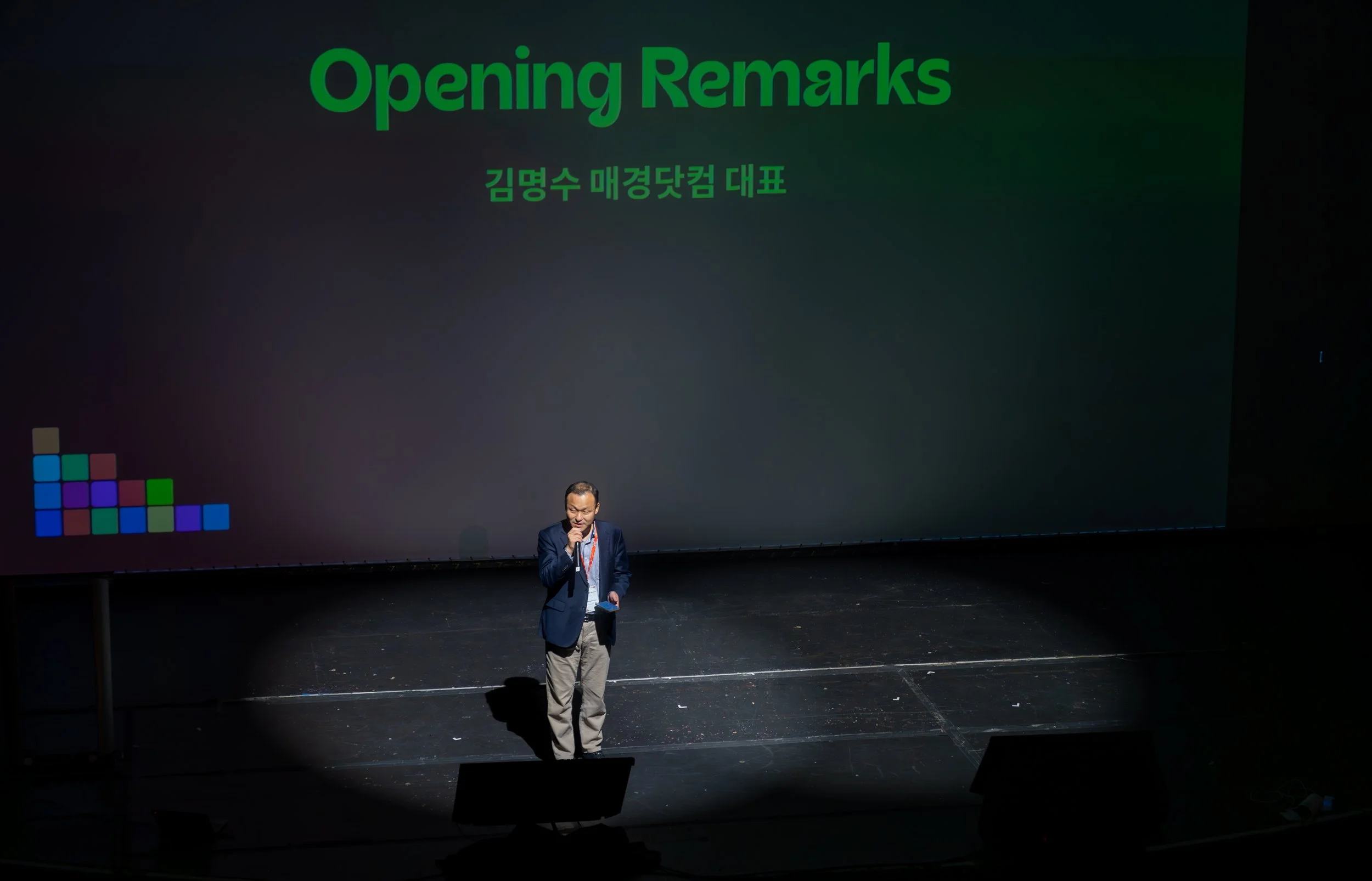 A speaker on stage giving opening remarks at a conference, with a large screen behind displaying 'Opening Remarks' and text in Korean.