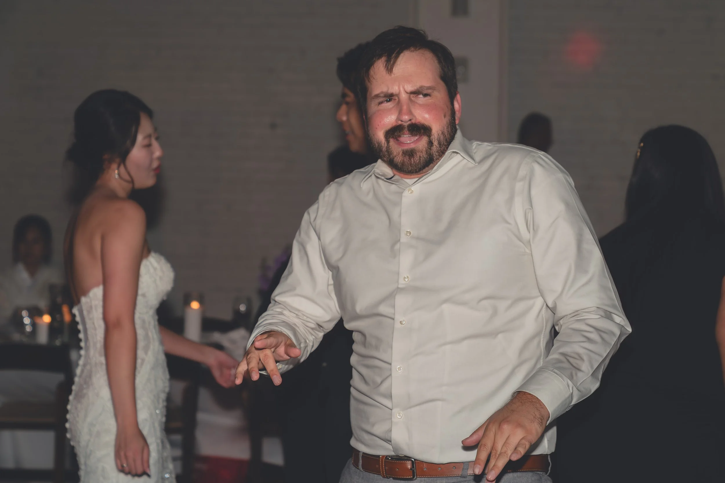 Man in a white button-up shirt dancing at an event with other people in the background.