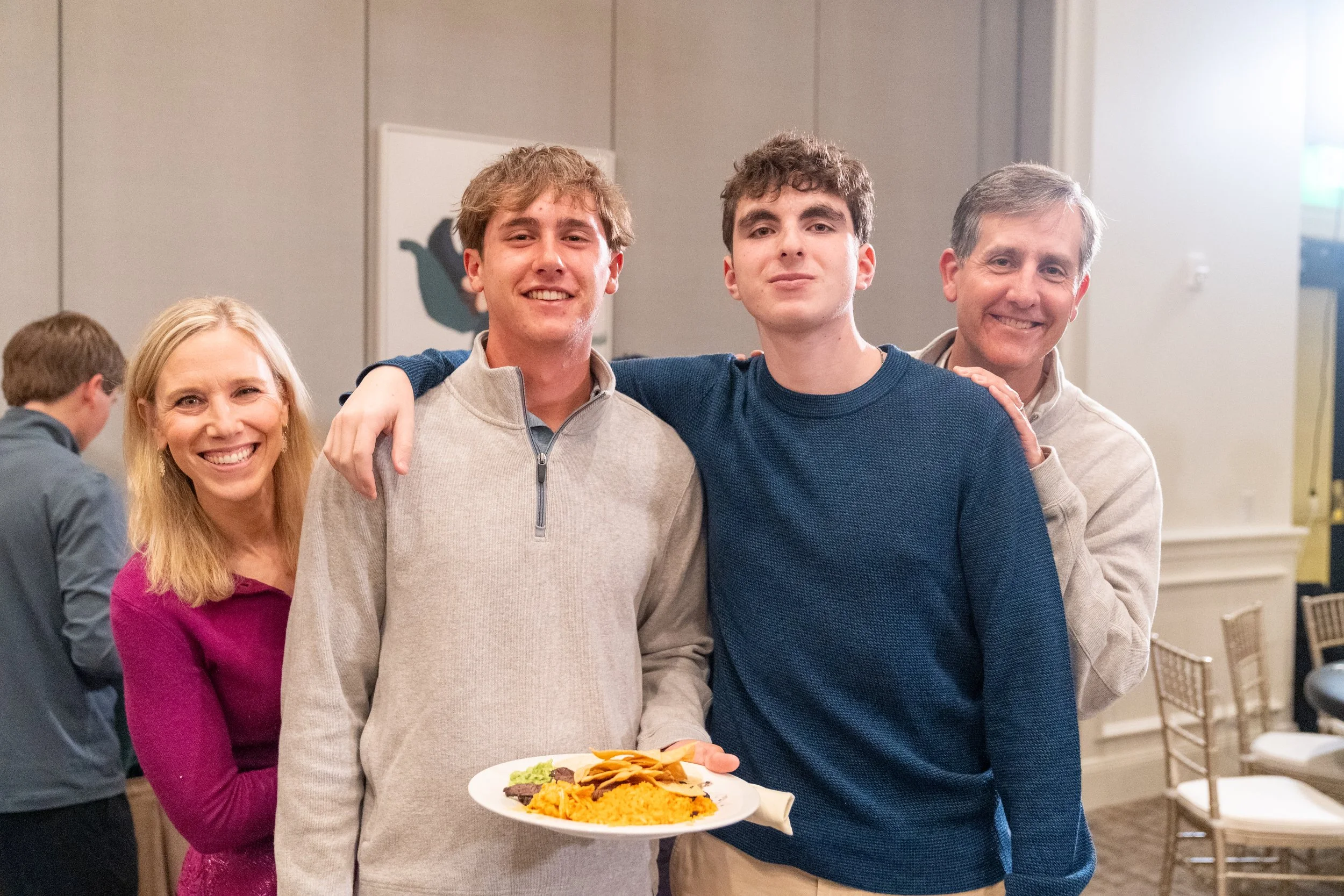Group of four people smiling at an event, with one person holding a plate of food.