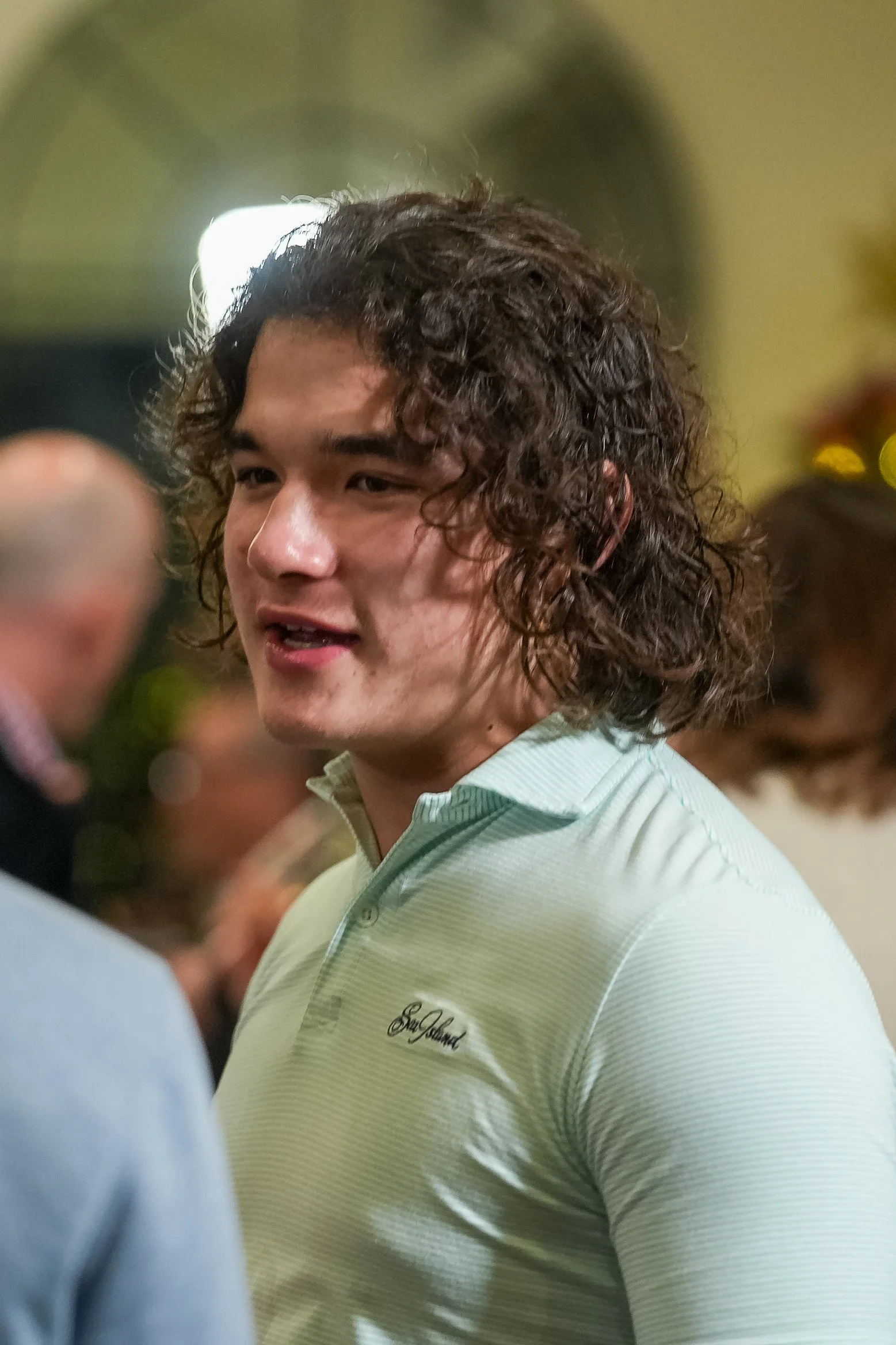 Young man with curly hair, wearing a light green collared shirt in a social setting.