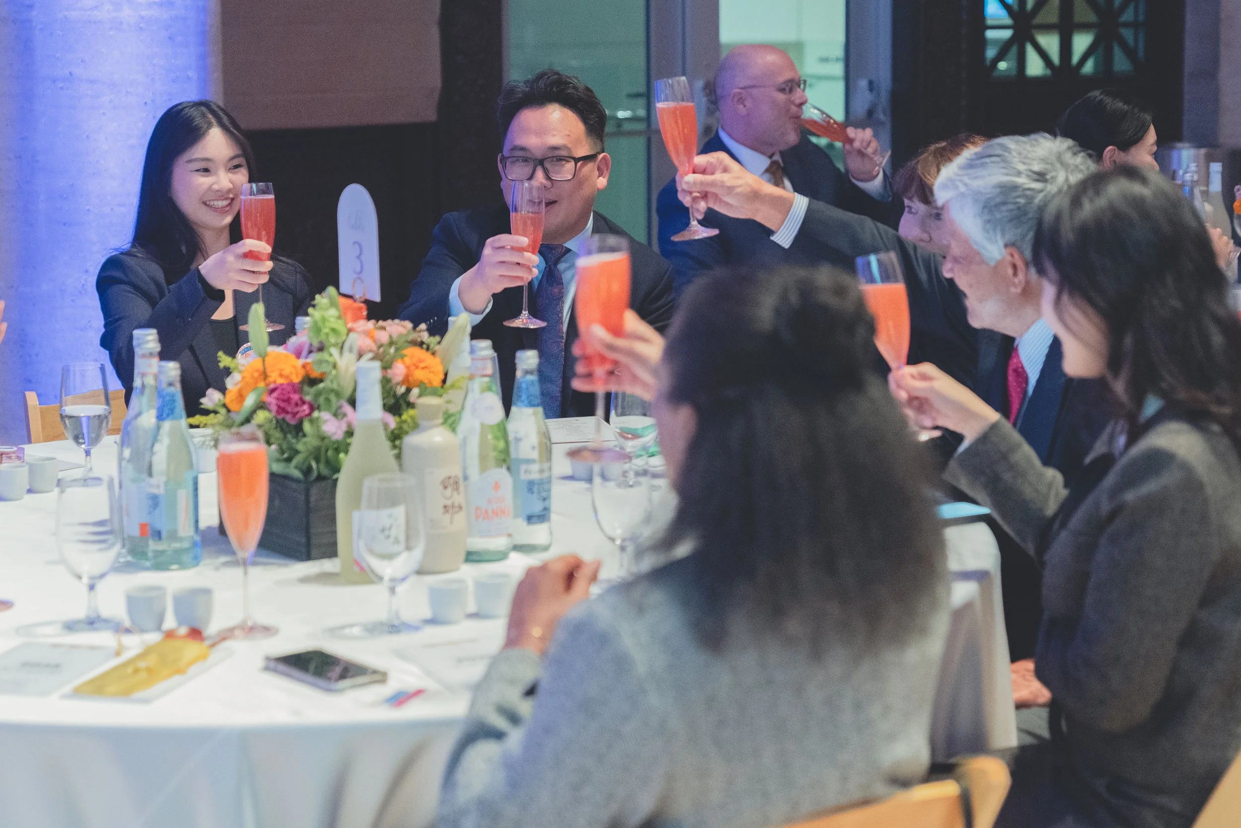 Group of people celebrating at a dinner party, raising glasses of pink champagne in a toast.