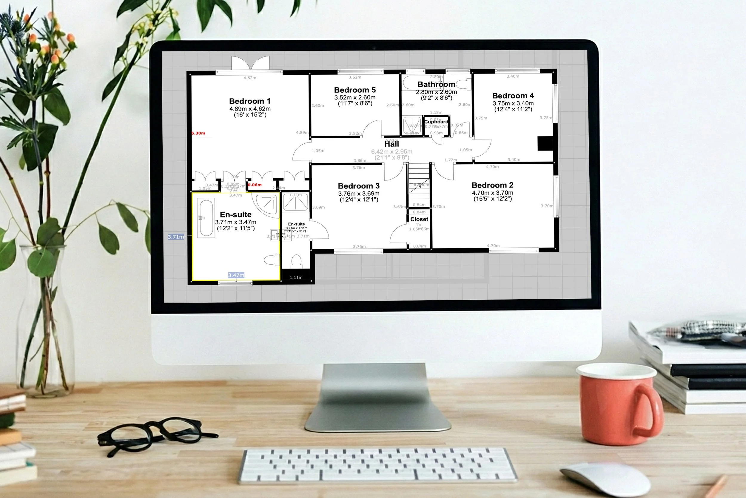 A professional five-bedroom house floor plan shown on a computer monitor sitting on a wooden desk with a coral mug in keyshoot brand colours and glasses.