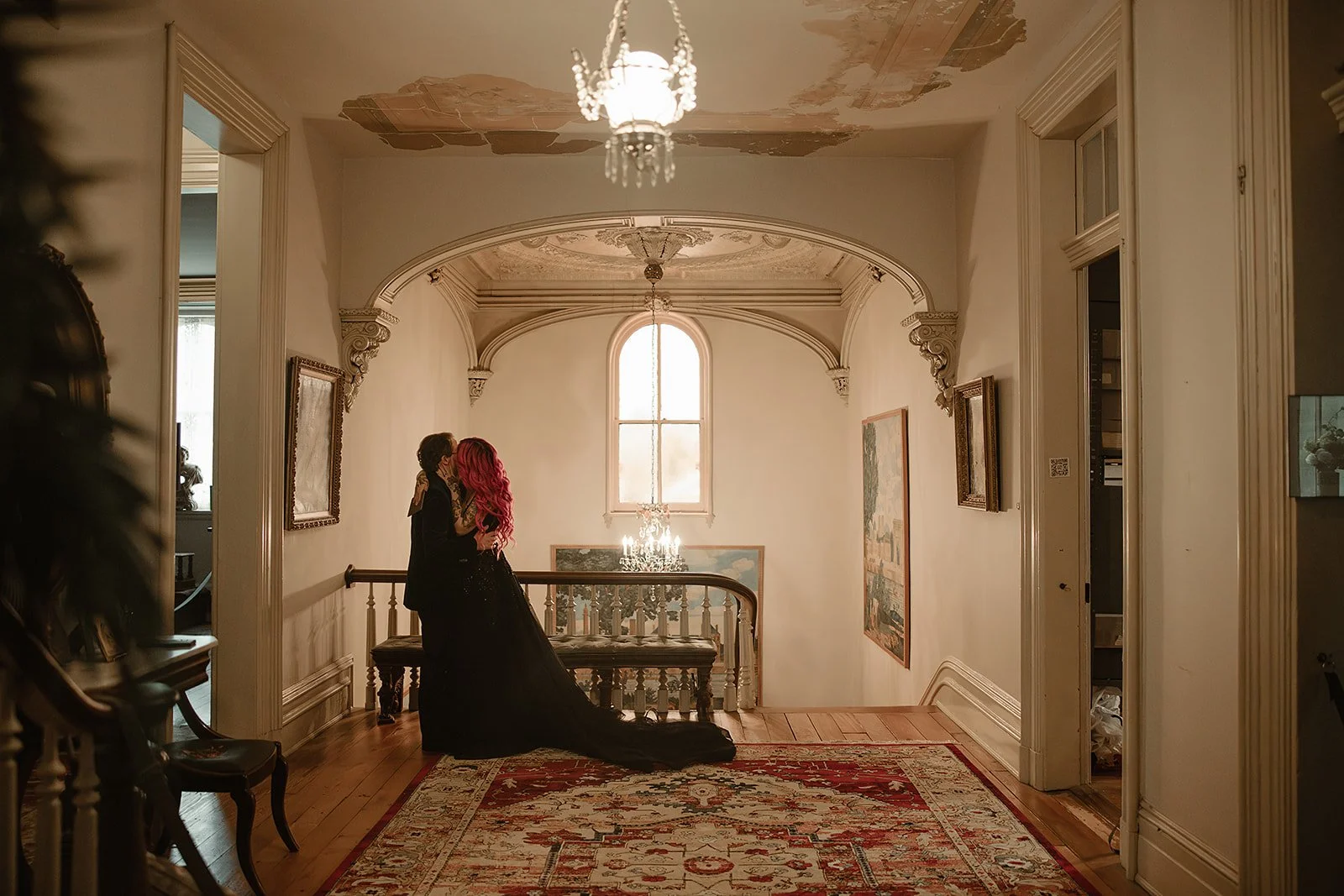 Married couple embrace and kiss on a staircase landing in an elegant, vintage-style home with ornate ceiling details, a chandelier, framed artwork. Woodruff Fontaine House Museum. Moody Wedding Photographer. Candid. Documentary timeless photographer