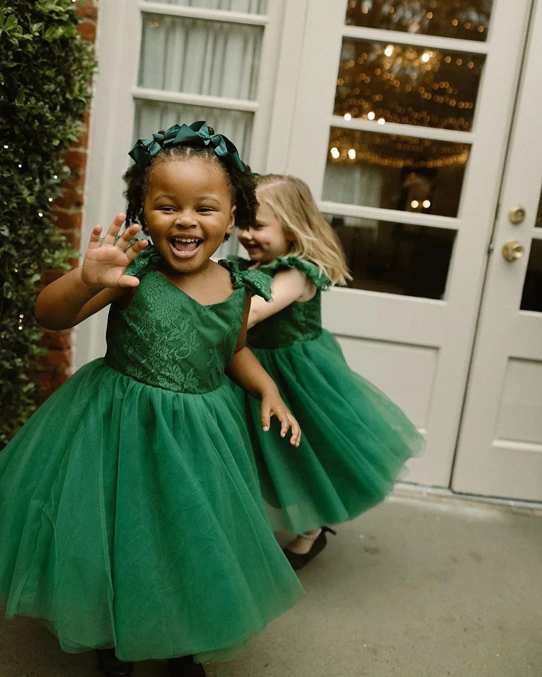 Two young girls in green dresses and hair accessories happily playing outside near a door.