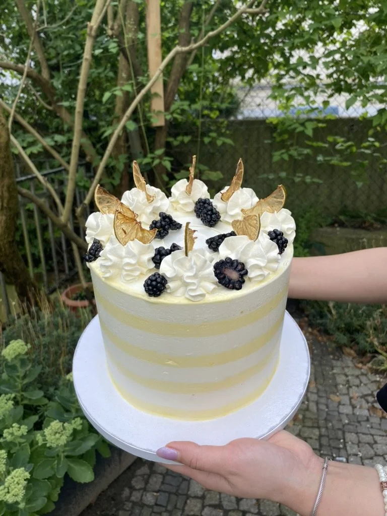 Gelb-weiß gestreifte Torte mit Sahnetupfen und dunklen Beeren