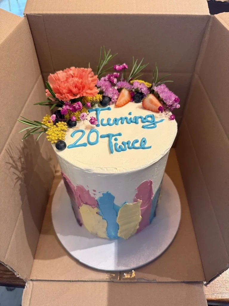 Torte mit blauem Schriftzug, bunten Blumen und Farbakzenten im Karton