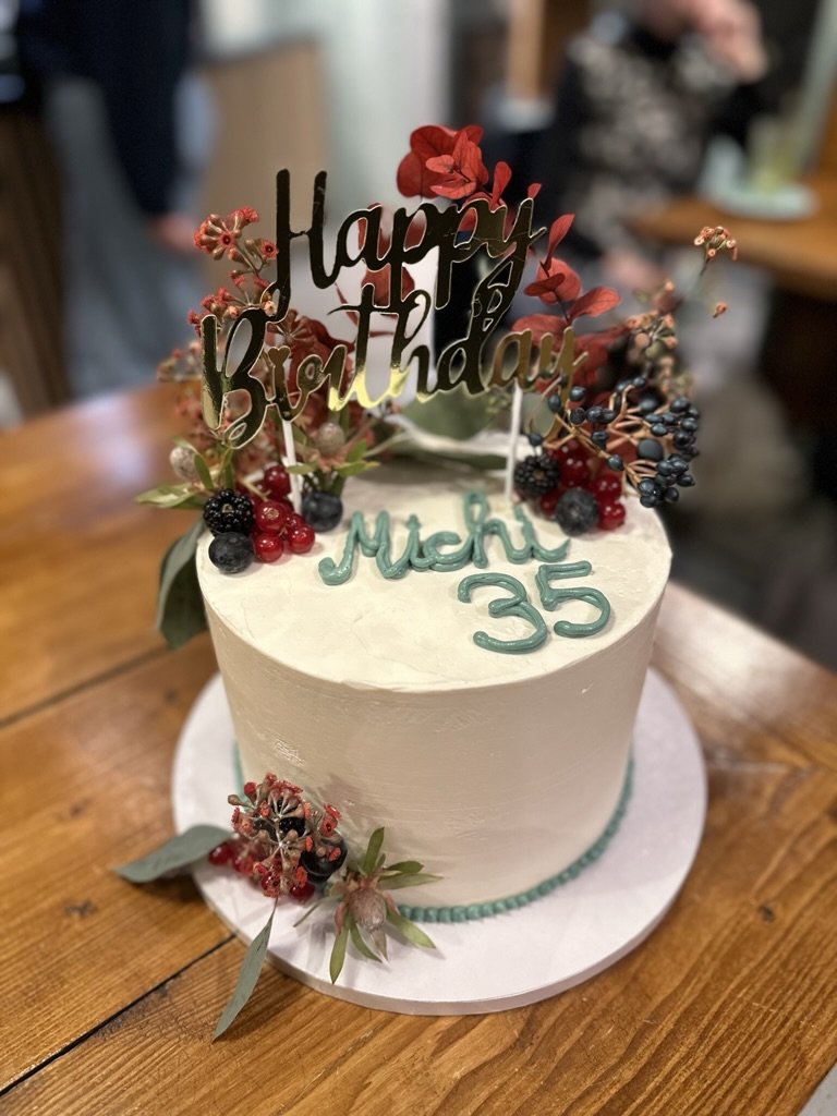 Weiße Torte mit dunkelroten Blumen, Schriftzug und Happy-Birthday-Topper