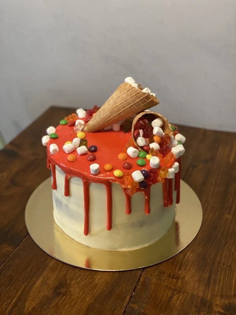 Weiße Torte mit rotem Drip, Waffeltüte und Süßigkeiten