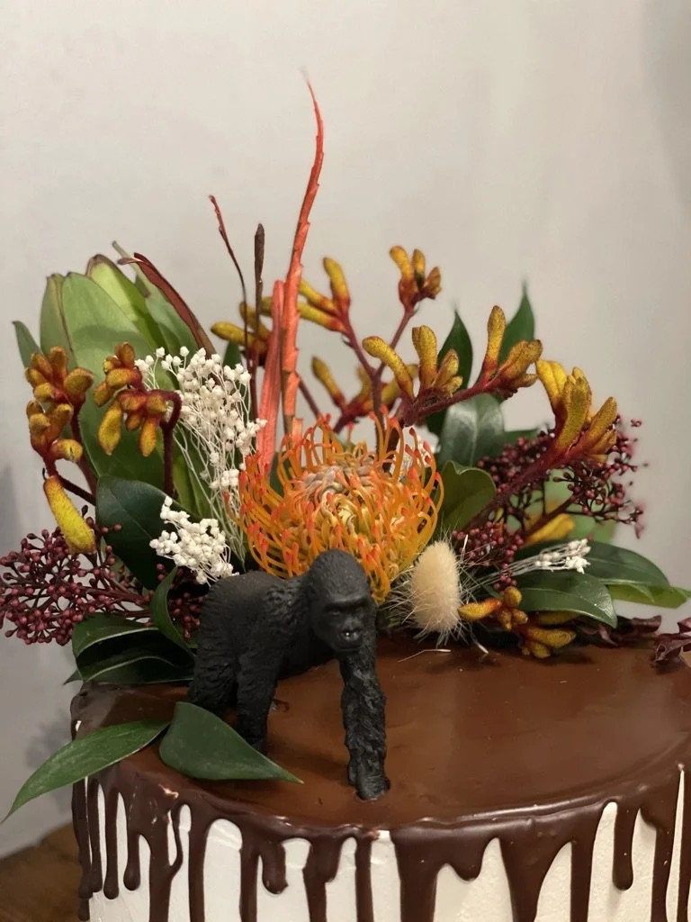 Nahaufnahme: Gorilla-Figur zwischen exotischen Blumen auf einer Schoko-Drip-Torte