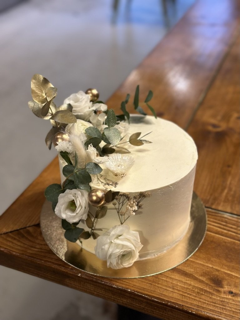 Weiße Torte mit weißen Blüten und goldenen Blättern auf einem Holztisch