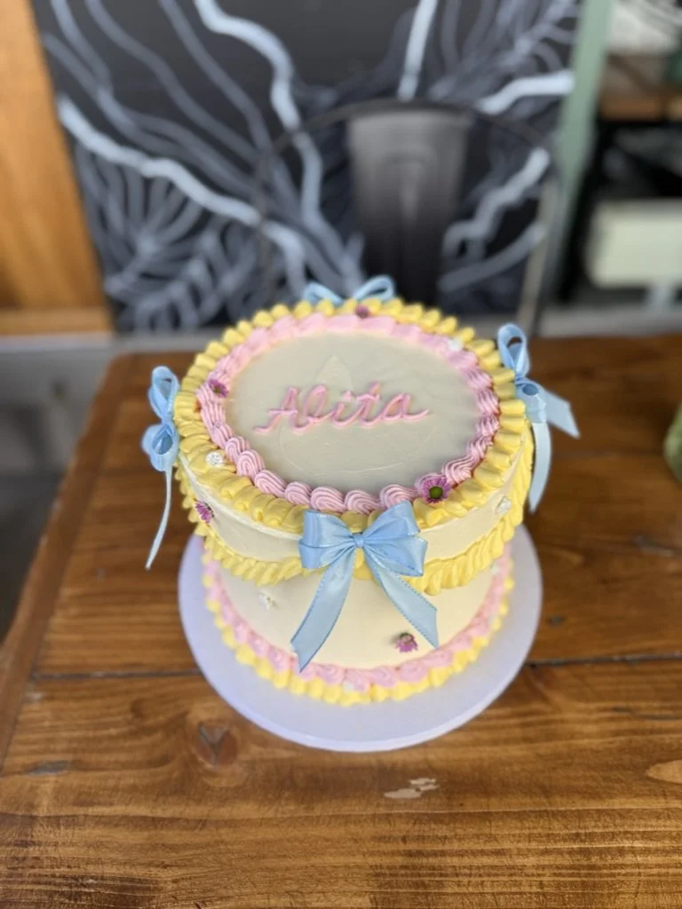 Vintage-Piping-Torte mit gelben und rosa Rüschen und blauen Schleifen auf einem Holztisch