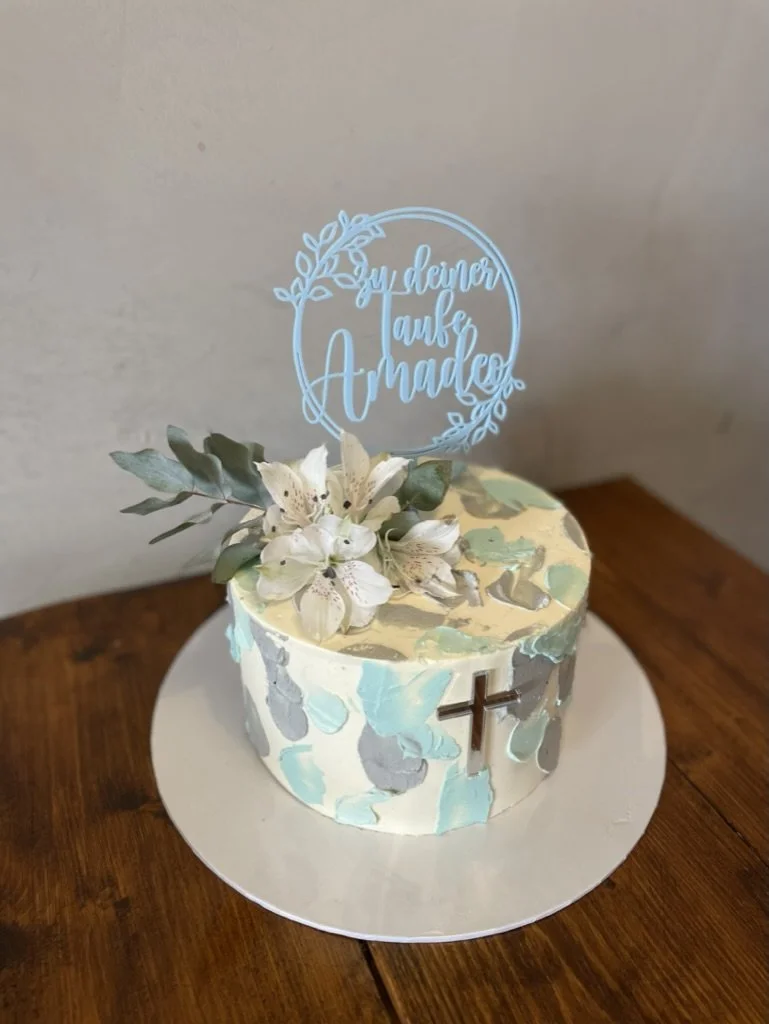 Tauftorte mit Kreuz, hellblauen Tupfen und Namens-Topper auf einem Holztisch
