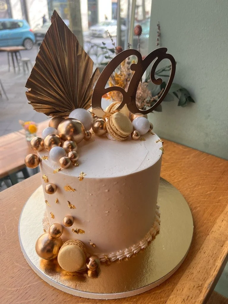 Weiße Torte mit goldenen Kugeln, Palmblatt und Zahl 60 auf einem Holztisch