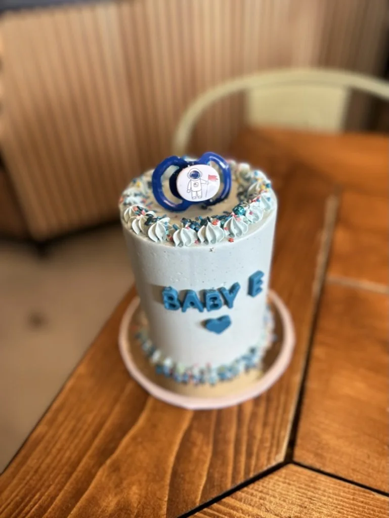 Hellblaue Torte mit Schriftzug und Schnuller-Deko