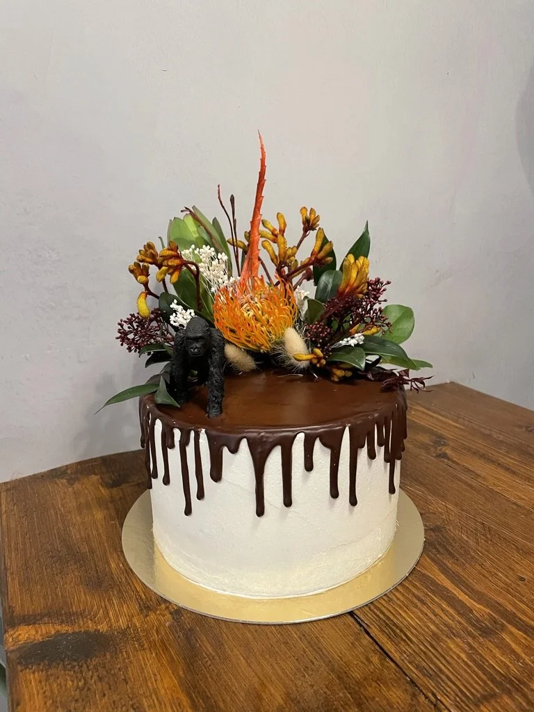 Weiße Torte mit Schoko-Drip, Tierfigur und exotischen Blumen