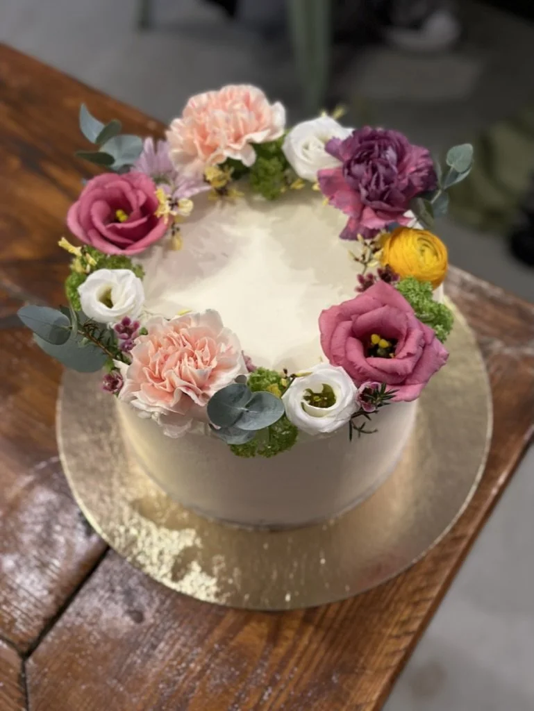 Weiße Torte mit Blumenkranz in Rosa und Pink