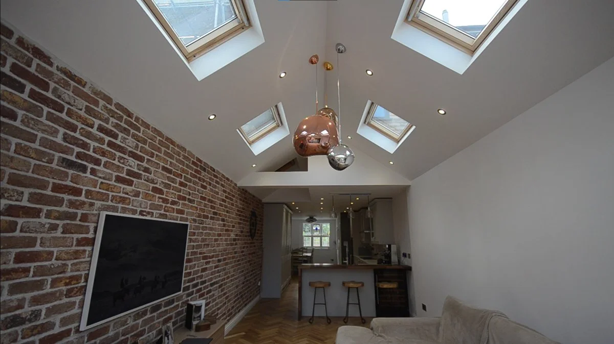 Raw Architects LTD — Living room with exposed brick wall, ceiling skylights, and modern copper and metallic pendant lights.