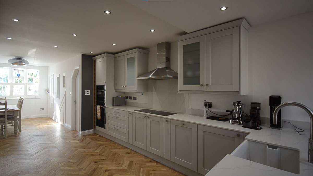 Raw Architects LTD — Modern kitchen with white cabinetry, marble countertops, stainless steel appliances, and light wood flooring, featuring a breakfast dining area near a