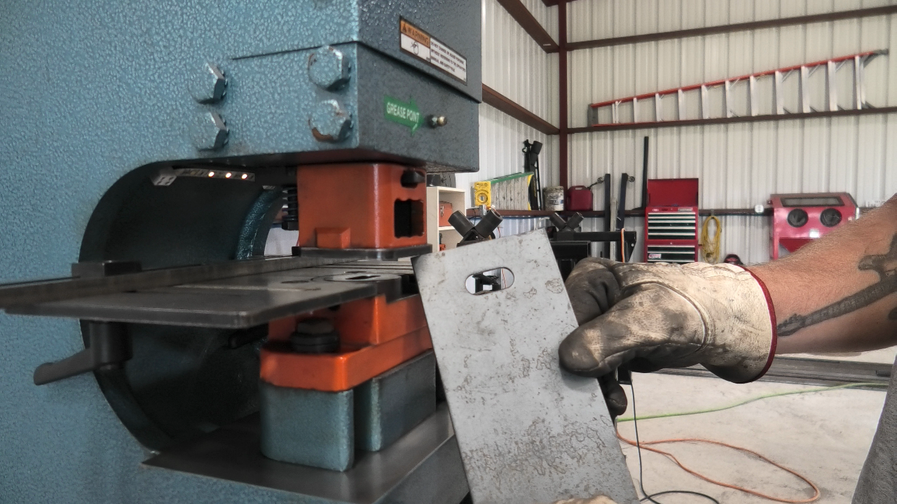 Person operating a metalworking machine with a gloved hand holding a metal sheet, inside an industrial workshop setting.