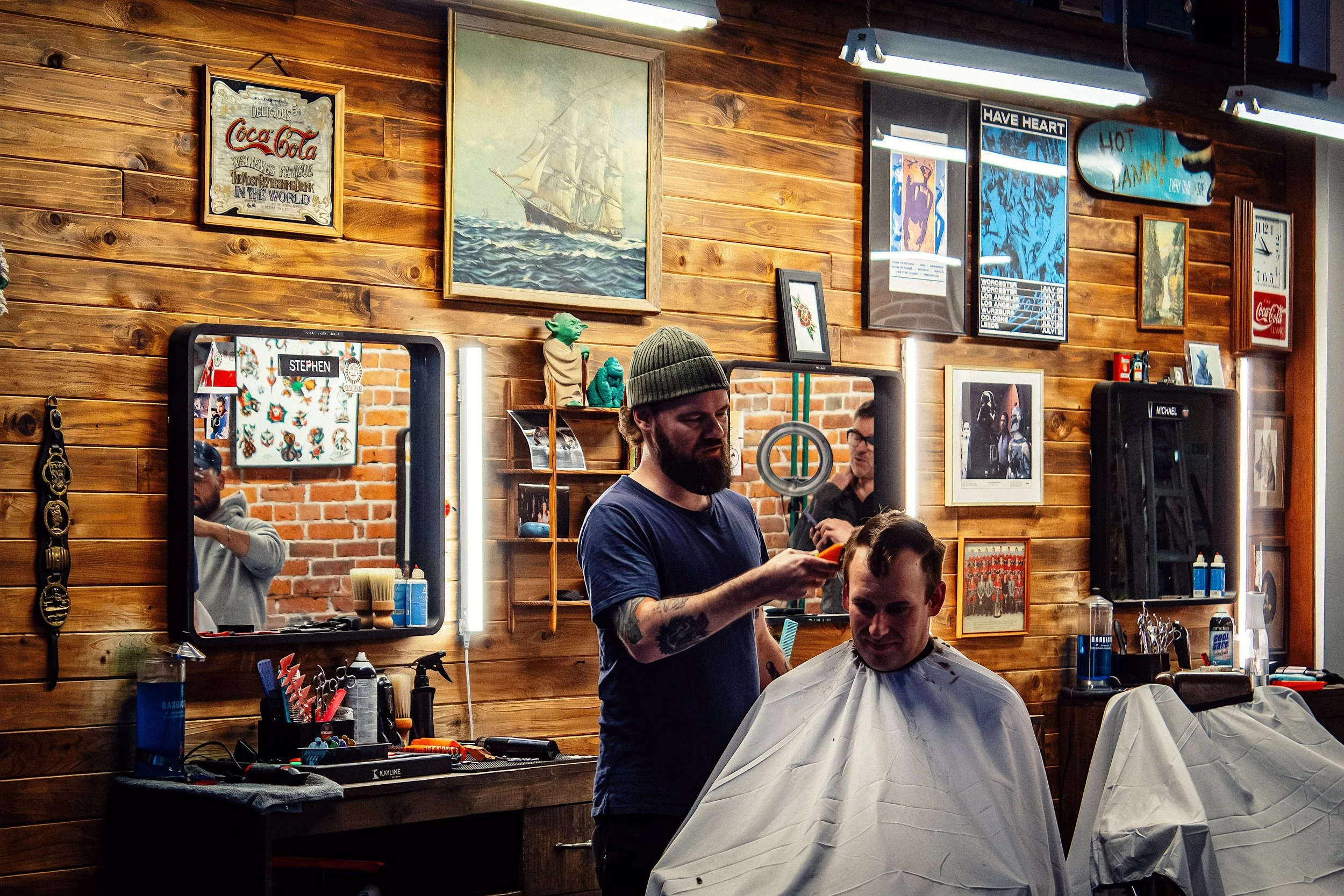 A barber giving a haircut to a man sitting in a barber chair, the barber shop is Rebellion Barber located in Victoria BC.
