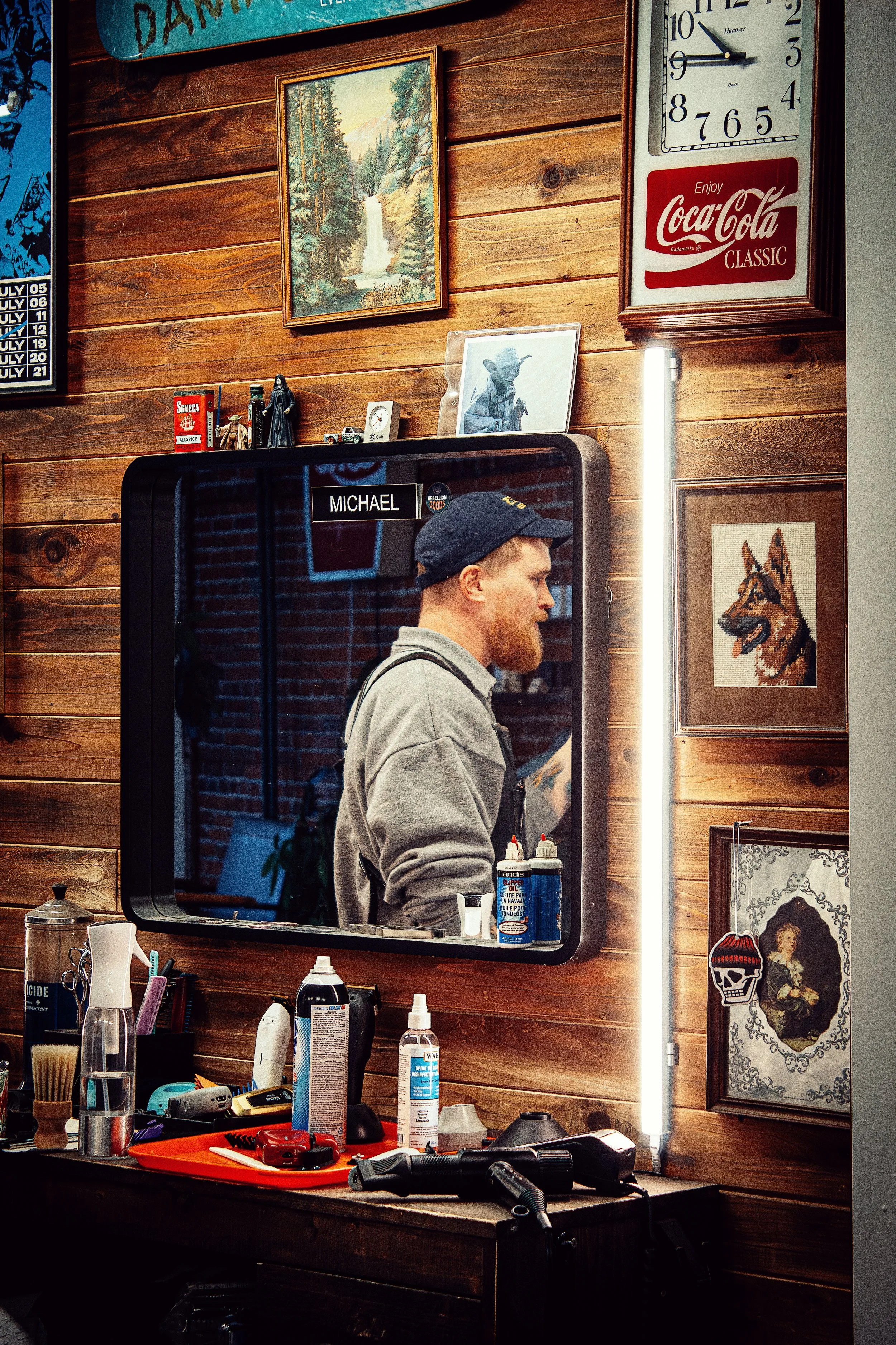The owner of Rebellion Barber, Michael Bodie, standing in his barbershop, his reflection showing in his barber station.