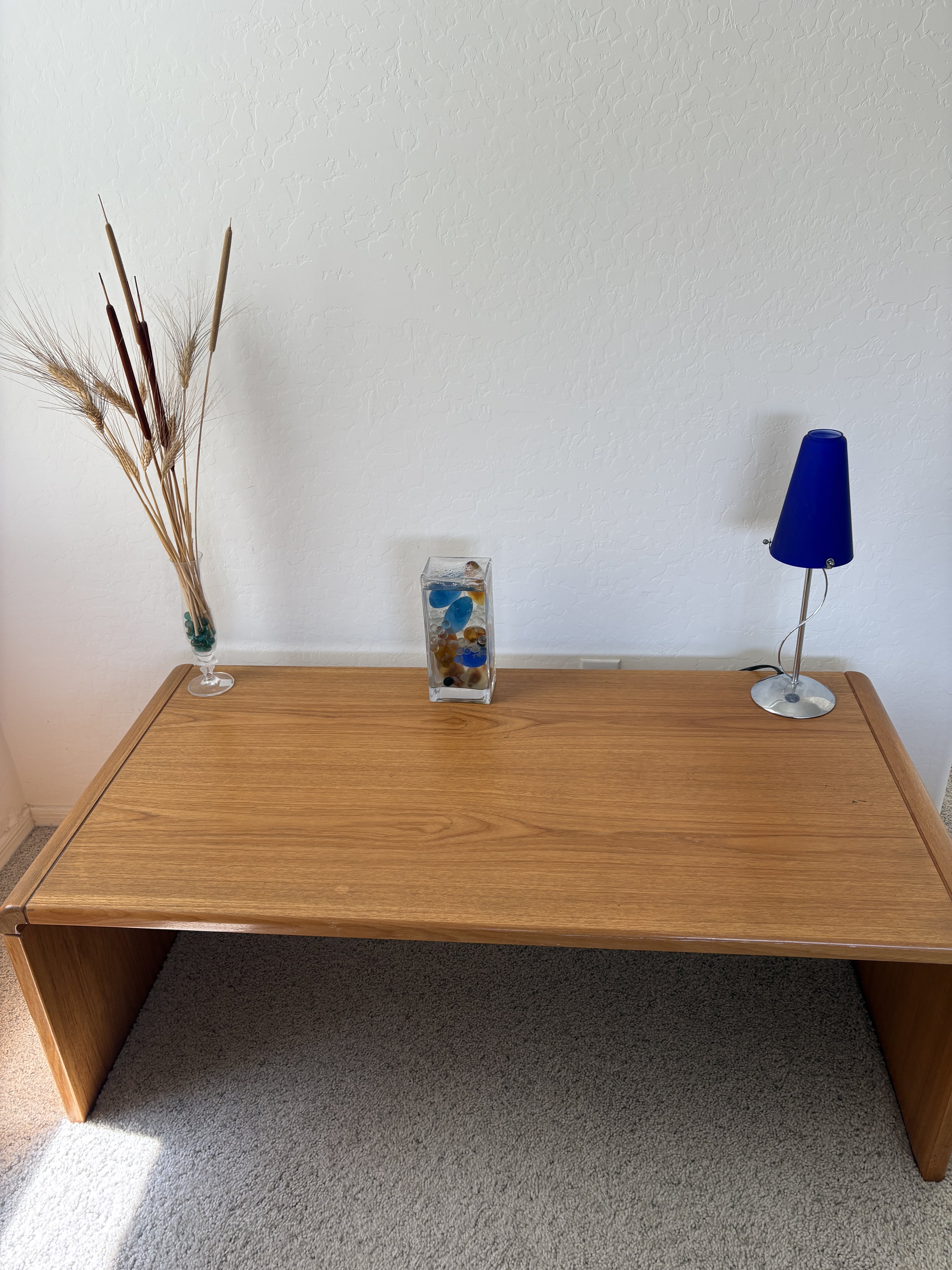 Wooden table with decorative vase, dried grass arrangement, and blue lamp