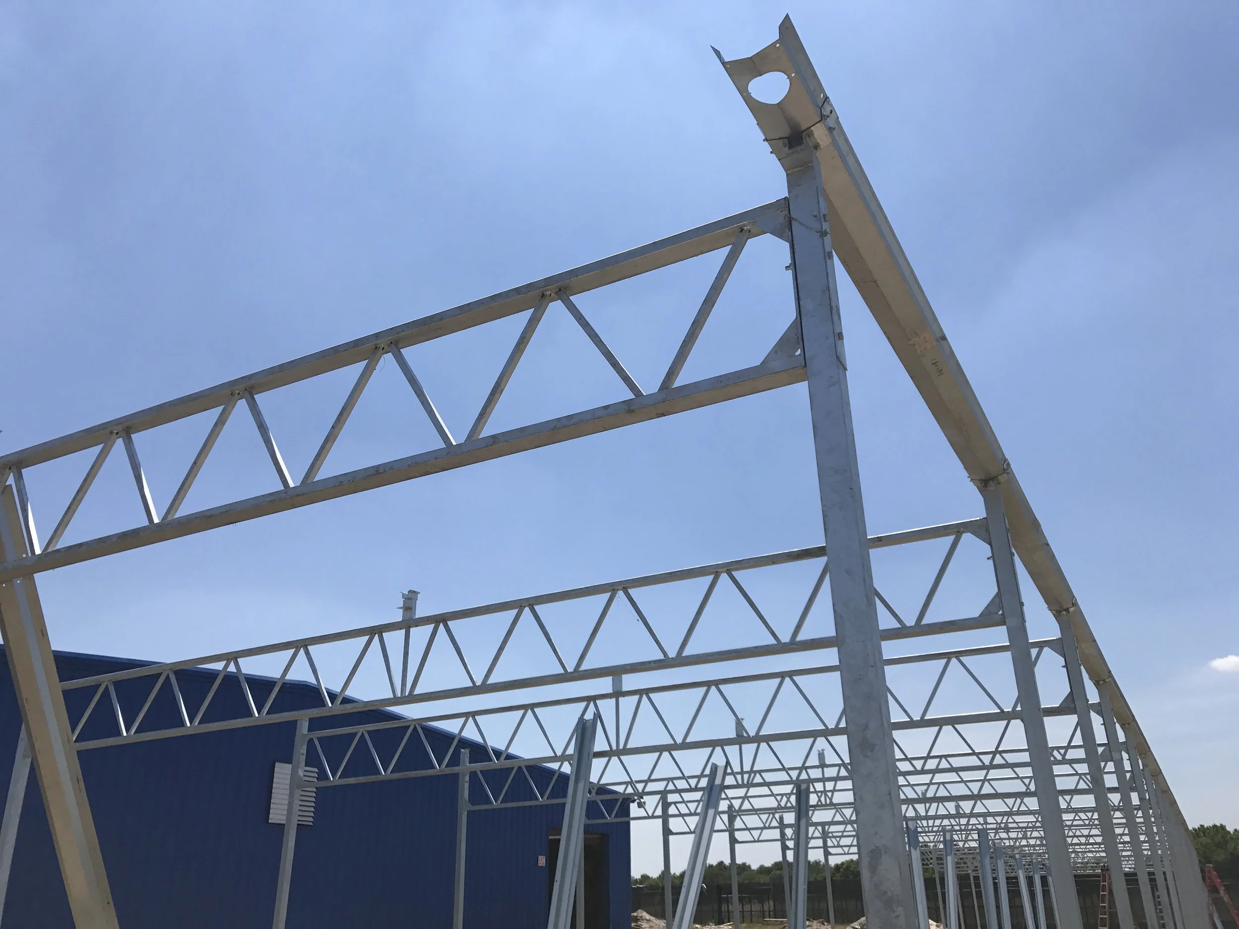 Metal framework of a building under construction against a clear blue sky.