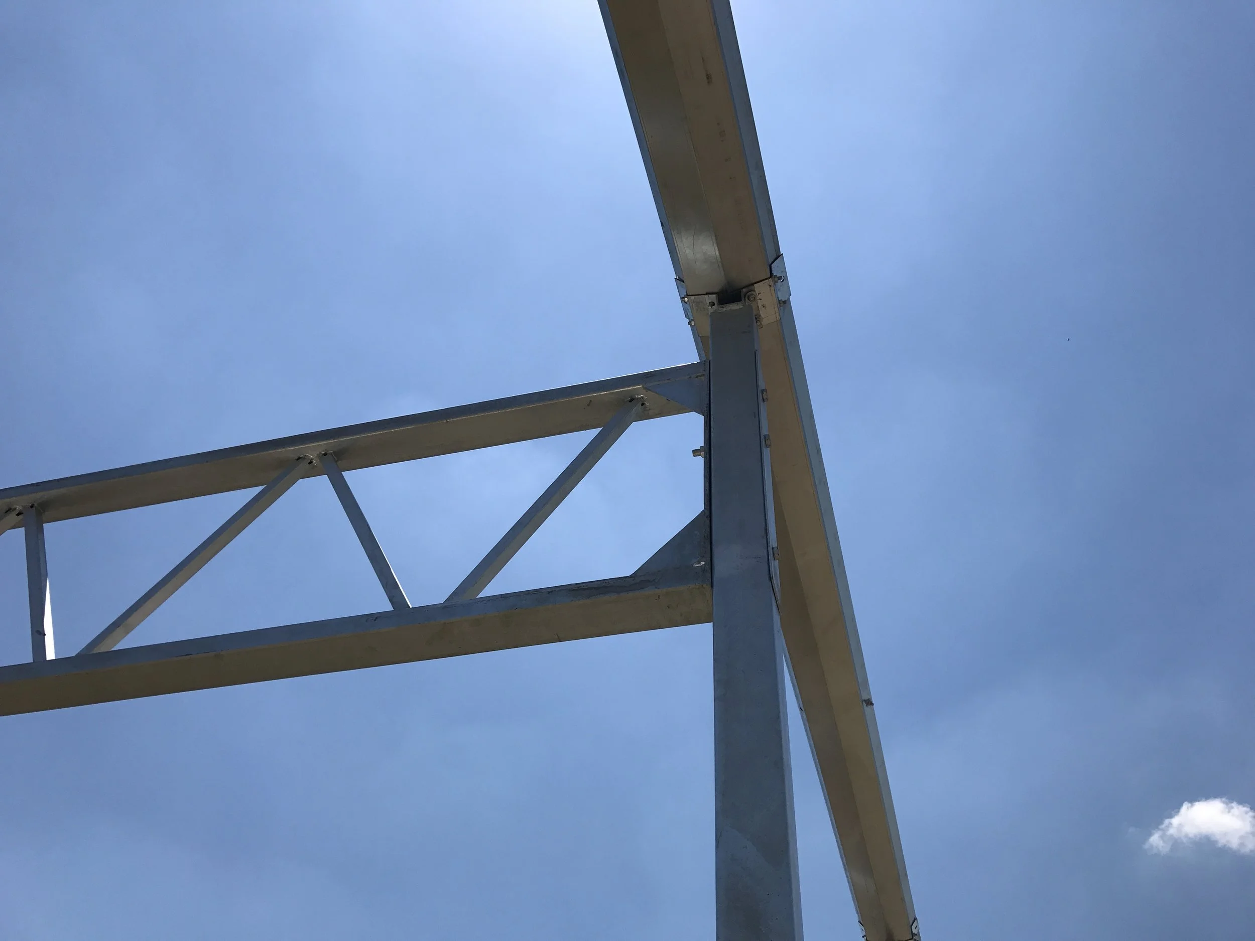 Upward view of a metal structure against a blue sky with a small white cloud.