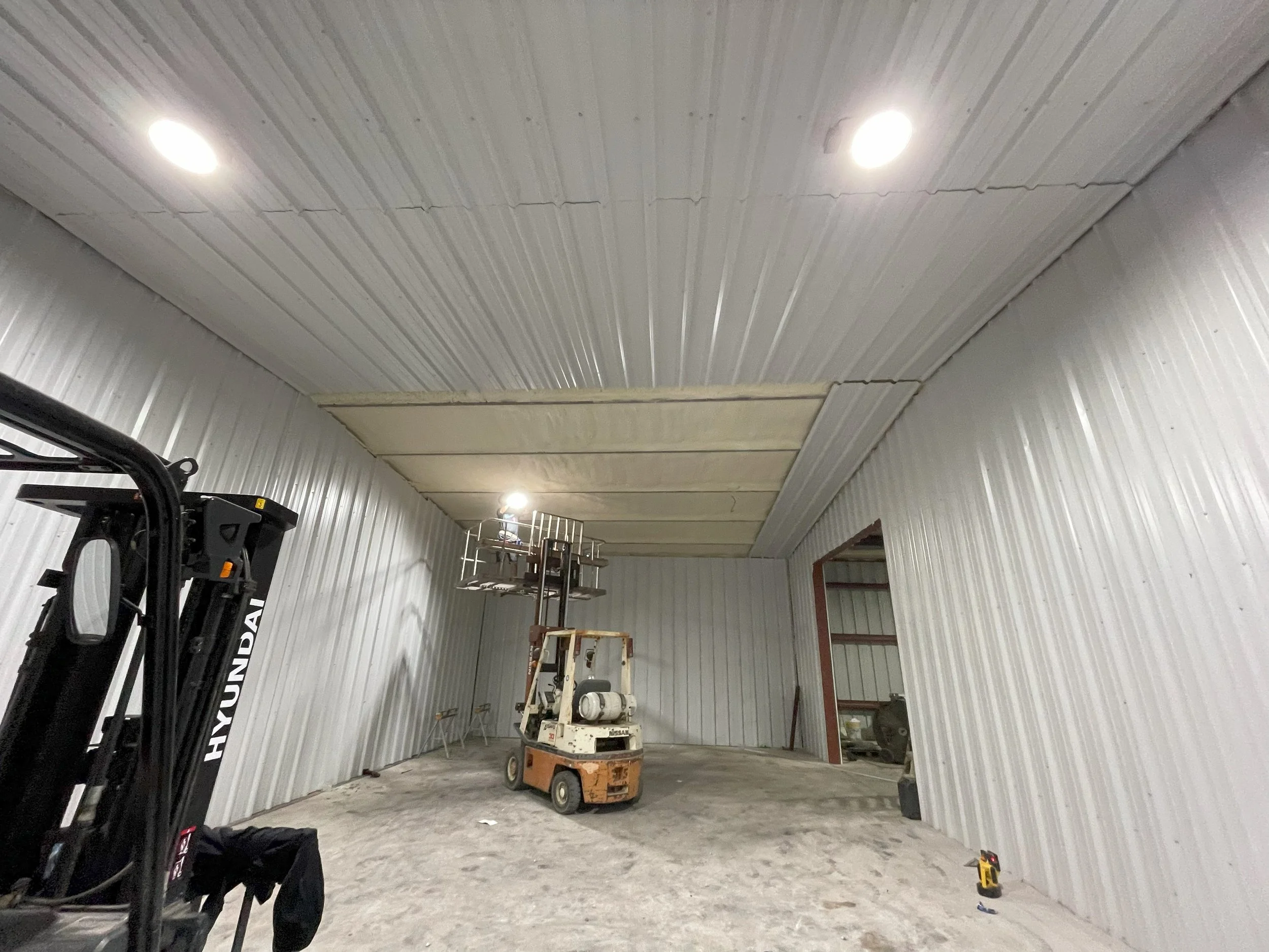 Construction site with metal walls and ceiling, a lift, and workshop equipment.