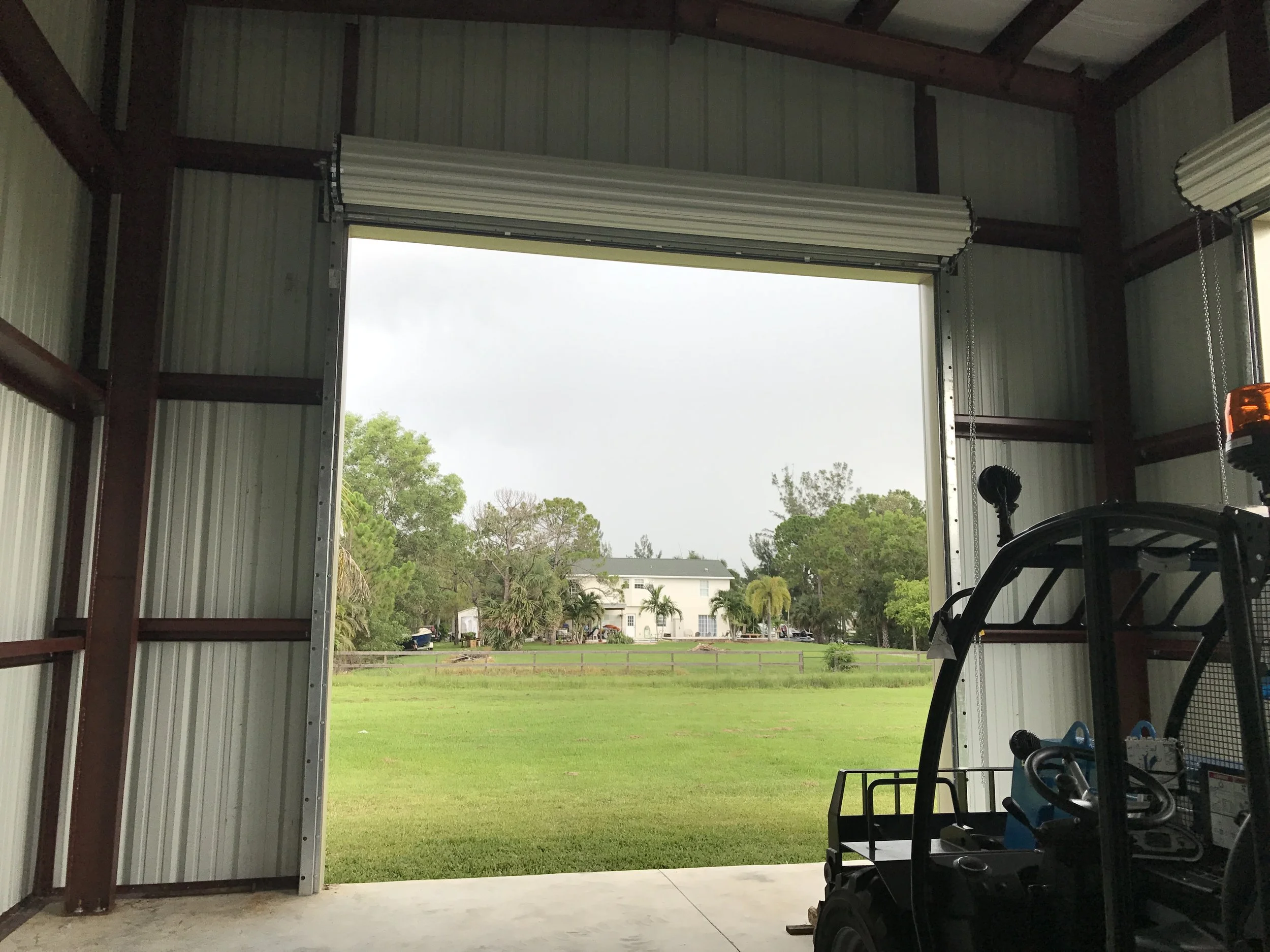 View of a green lawn and trees through a partially open industrial garage door, with a small utility vehicle parked inside.