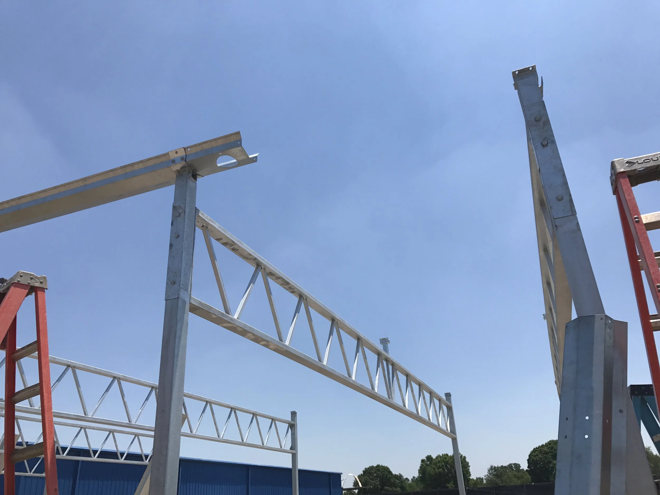 Metal framework structure under blue sky with trees in the background during construction.