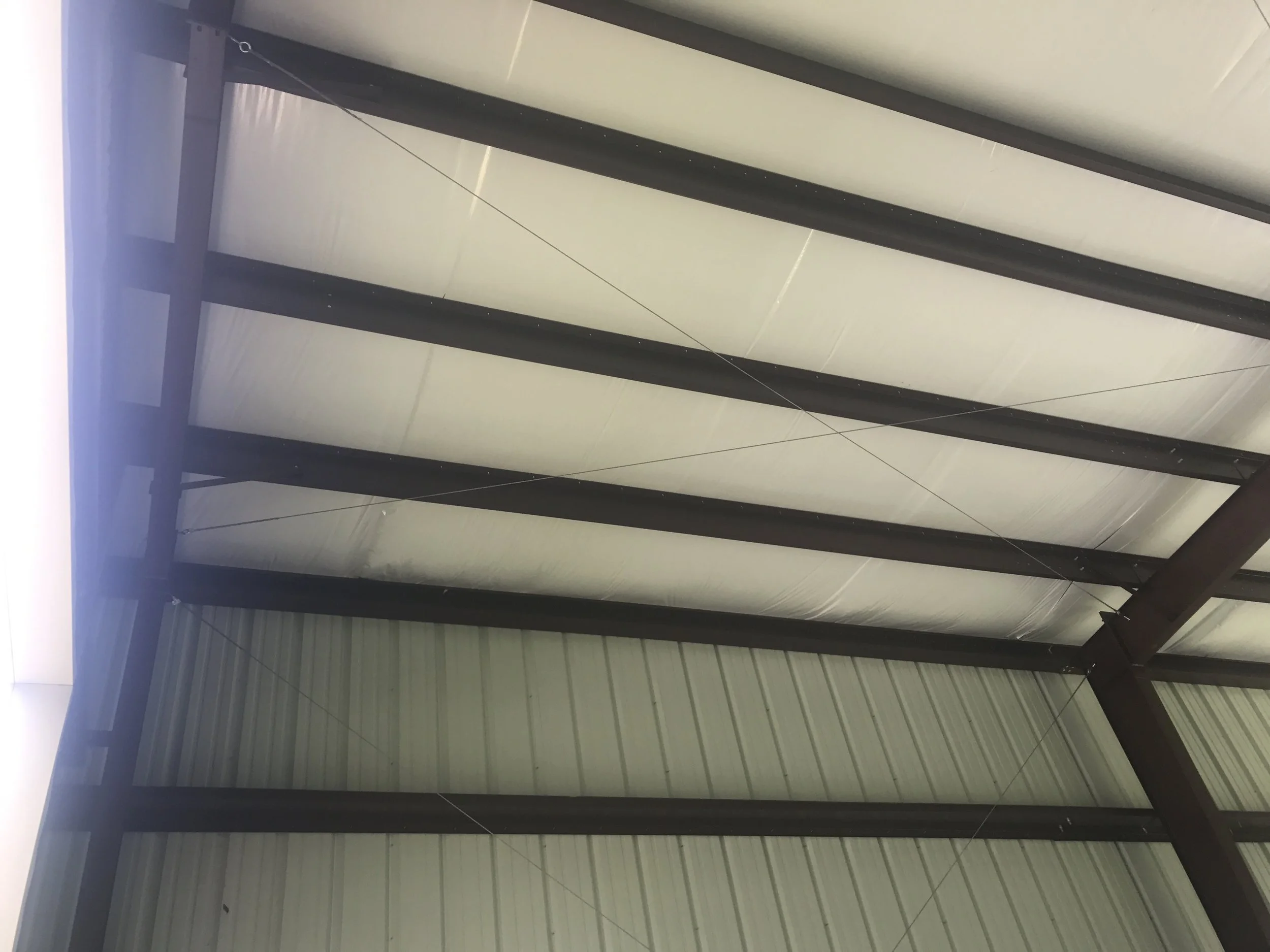View of the underside of a warehouse metal roof, featuring metal beams and panels.
